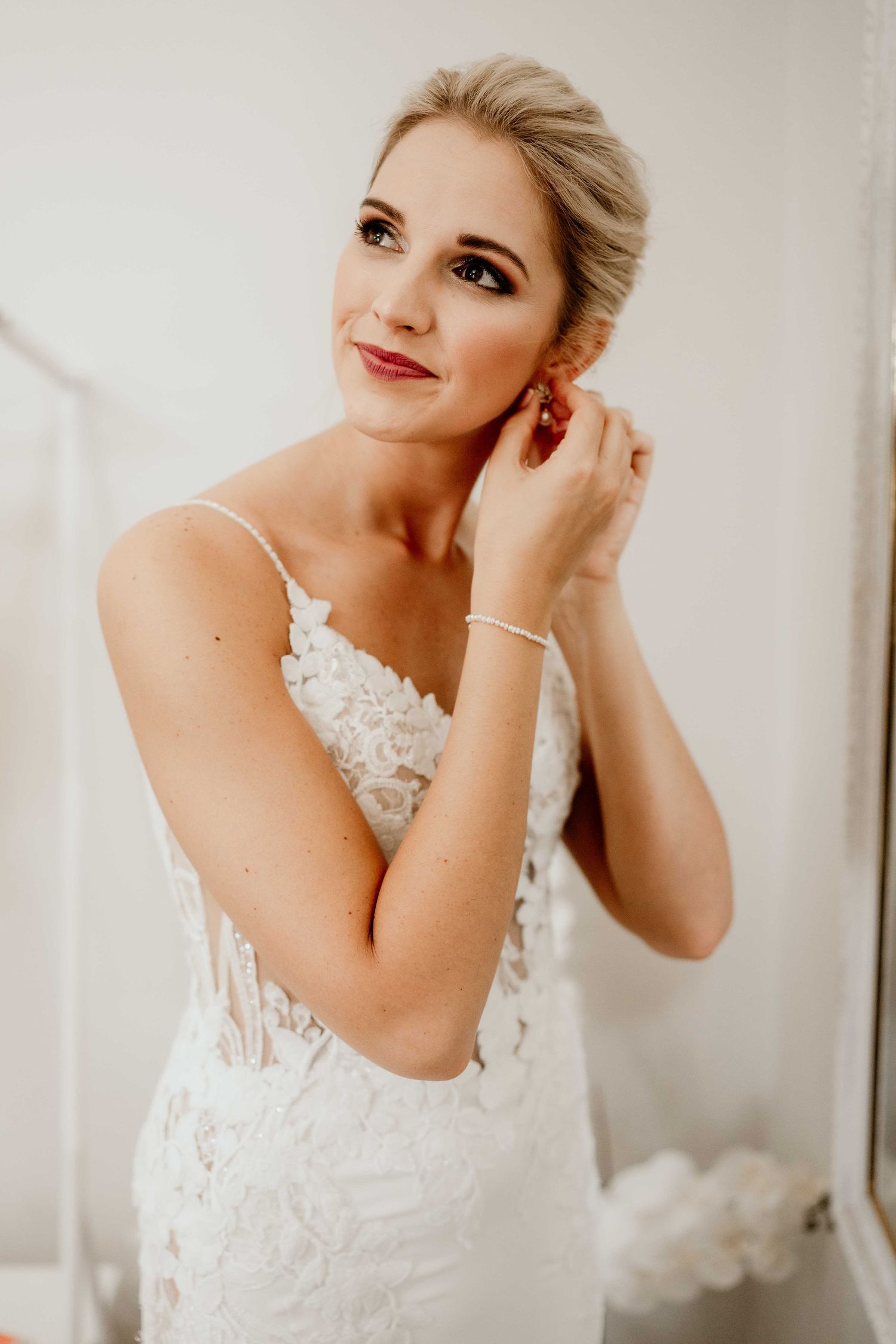 Beautiful bride wearing a lace wedding dress with delicate details poses elegantly while getting ready.
