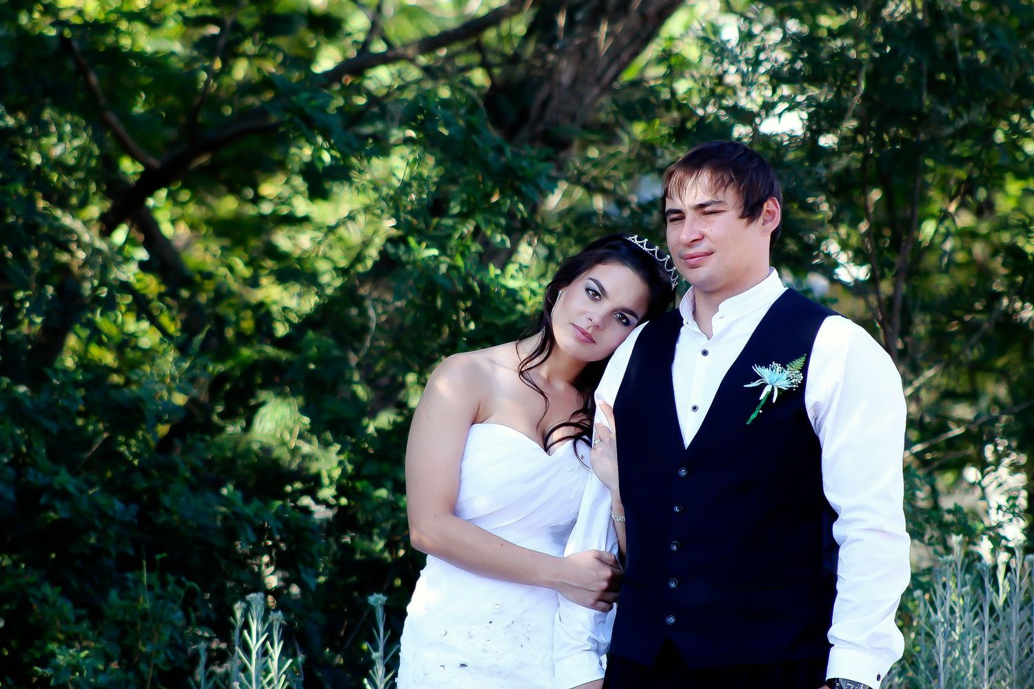 Romantic wedding couple poses together in a lush green garden setting.