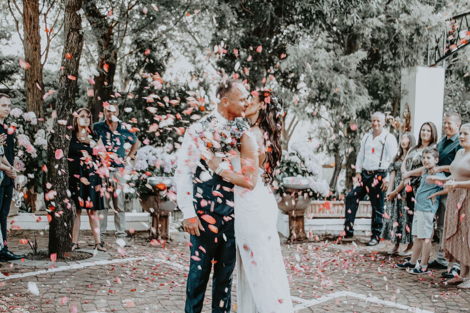 Newlyweds share their first dance surrounded by confetti and guests at an outdoor wedding ceremony.