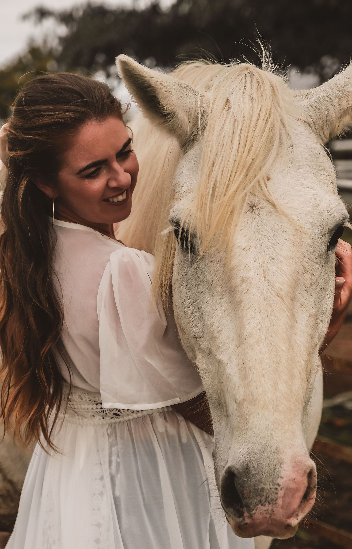 A white horse and someone in a white dress share a tender moment outdoors.