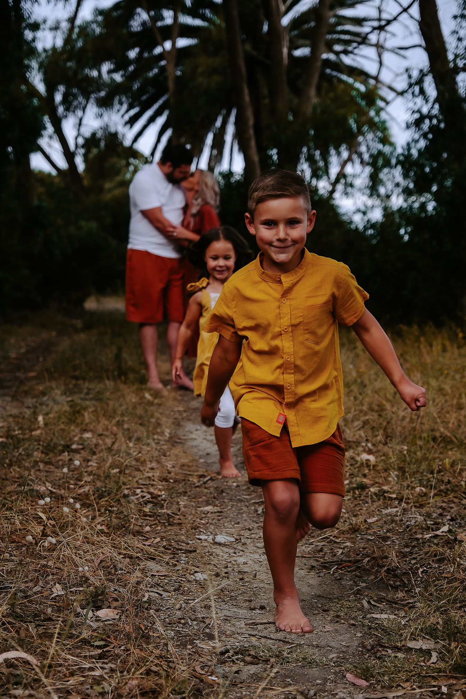 Child in a yellow shirt runs barefoot along a nature trail.