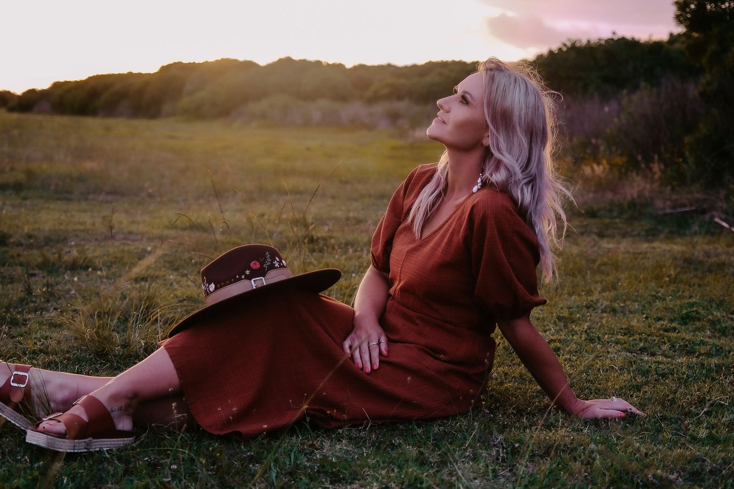 Woman in a rust-colored dress relaxes in a field during golden hour.