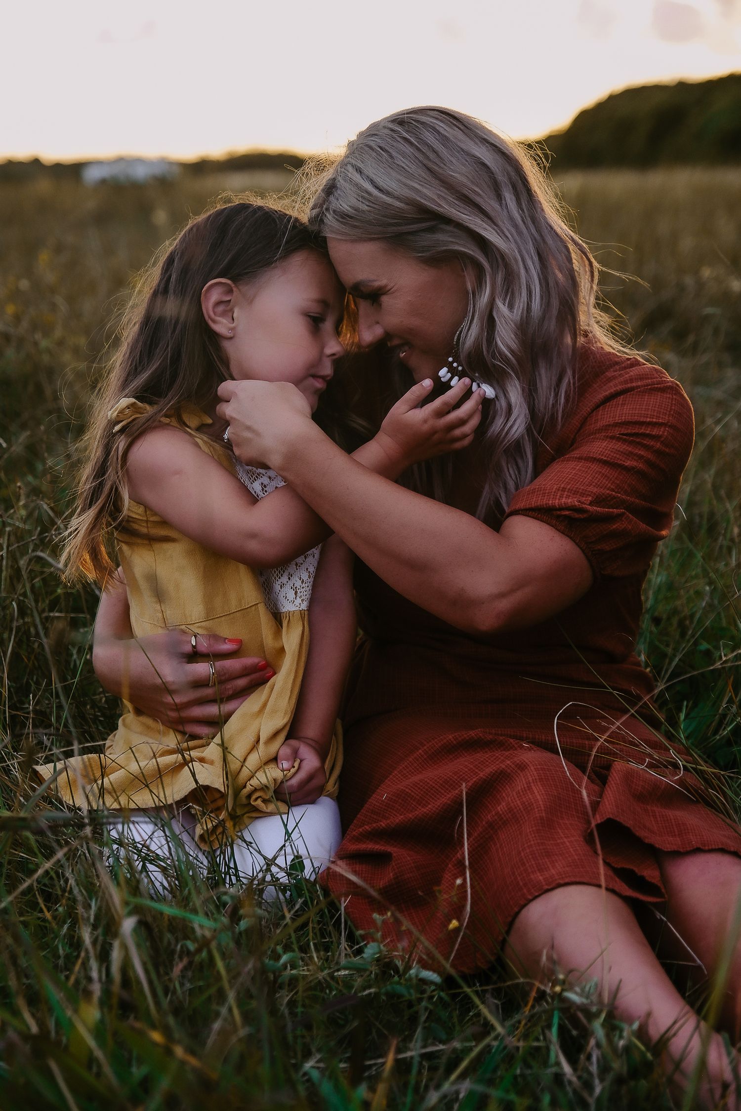 Touching moment between parent and child sitting in tall grass at sunset.