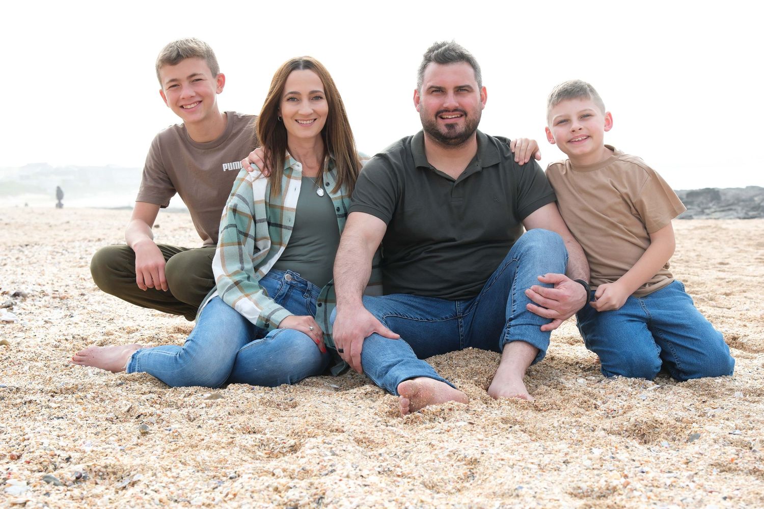 Small group sitting casually together on a pebbly beach with ocean in background.