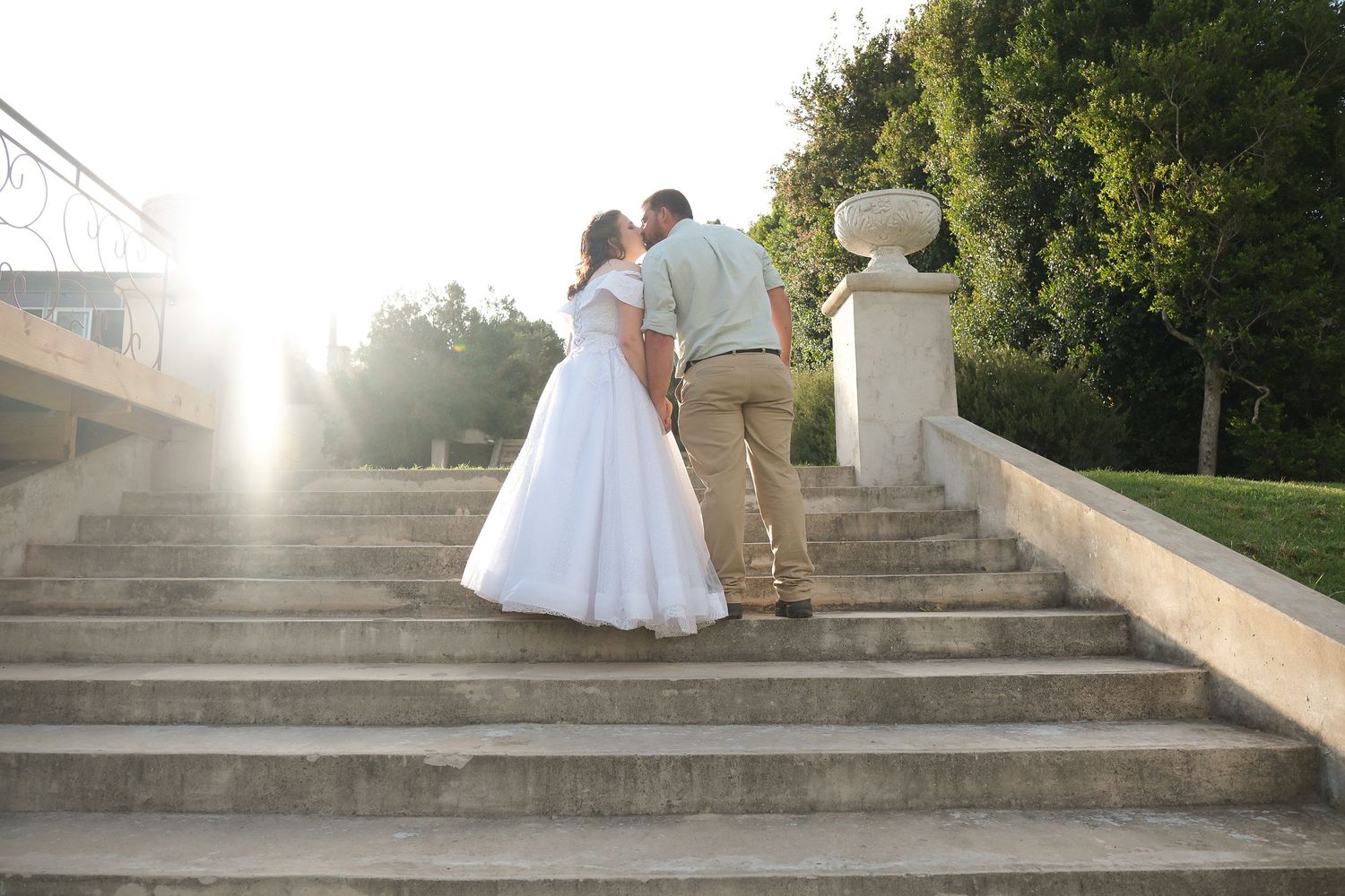 A wedding couple embraces on stone steps during golden hour.