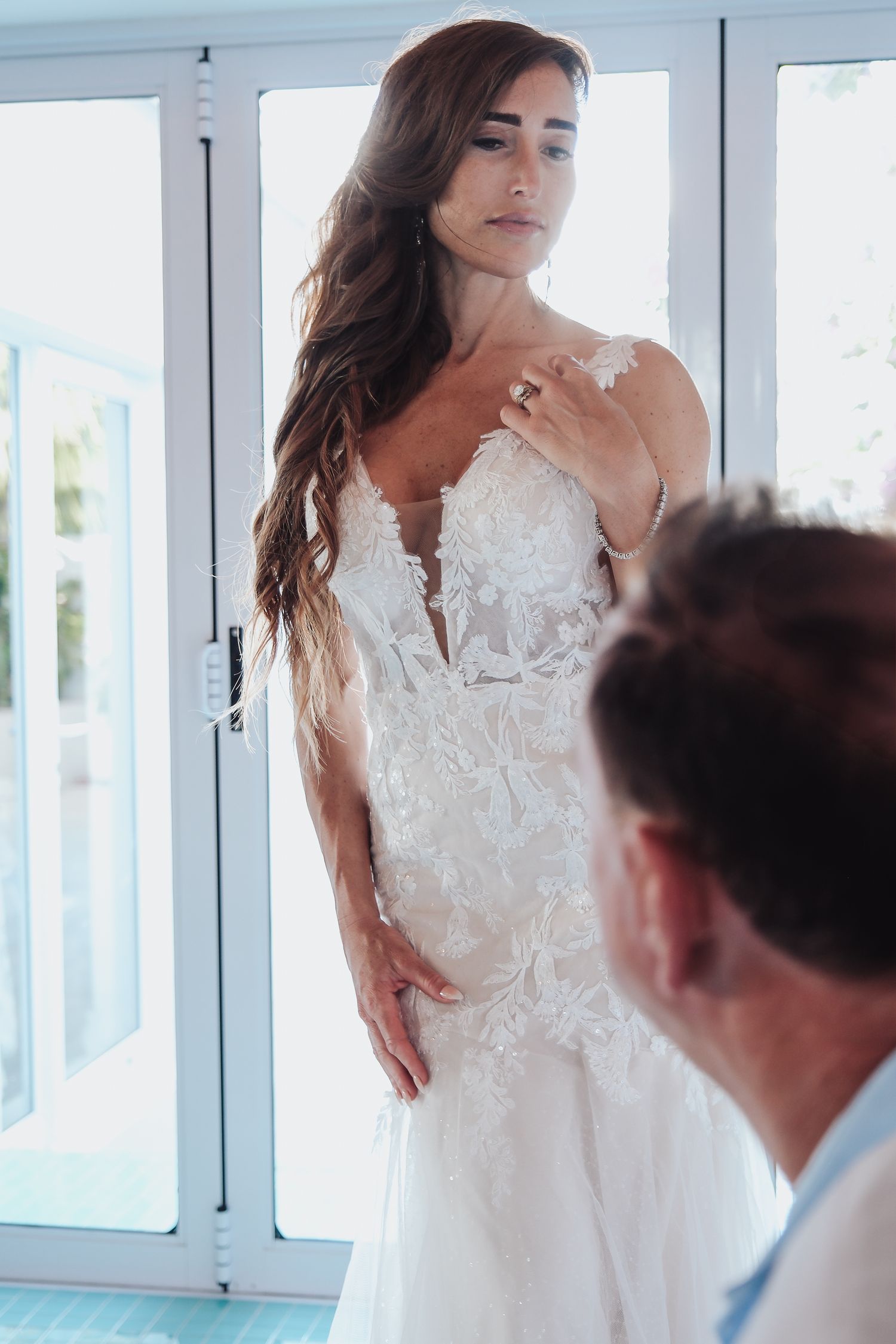 Dramatic bridal portrait featuring elegant white lace gown near bright windows.