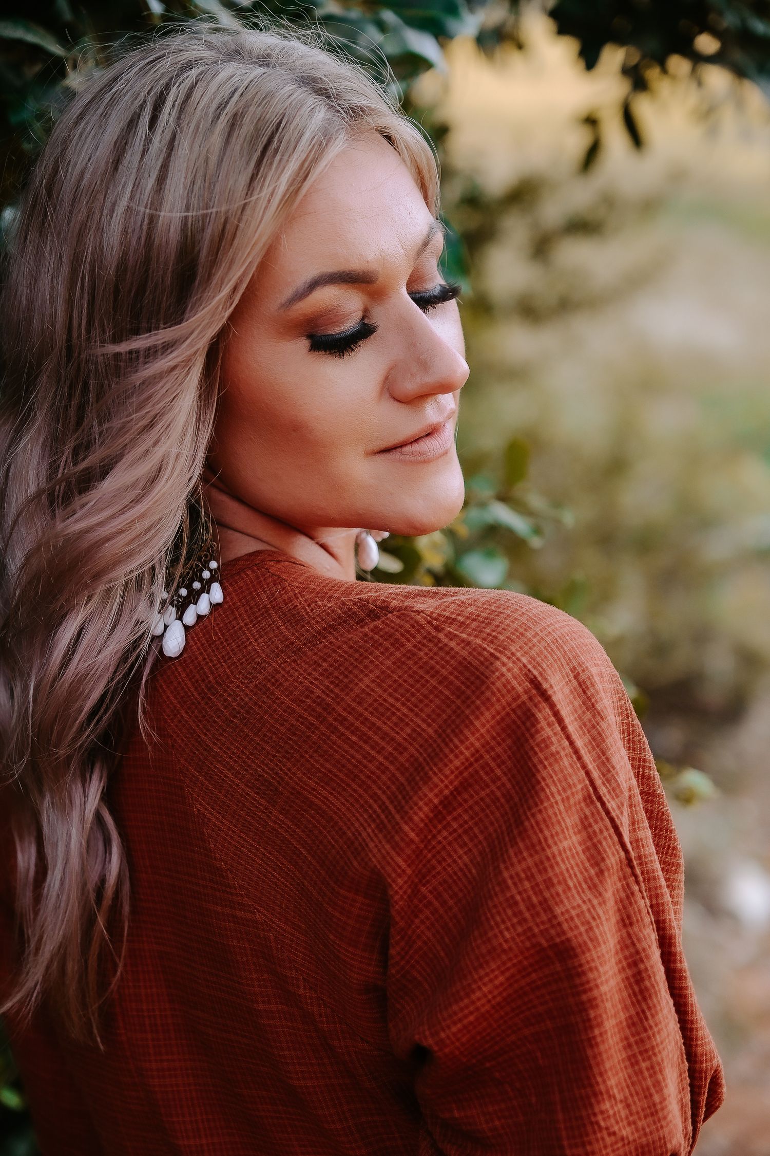 Side profile portrait of a woman with wavy hair wearing a rust-colored top and statement earrings.