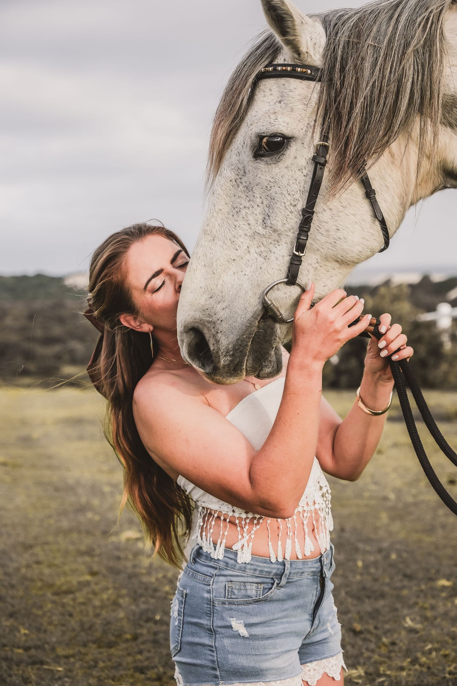 A white horse receives gentle affection outdoors against a cloudy sky.