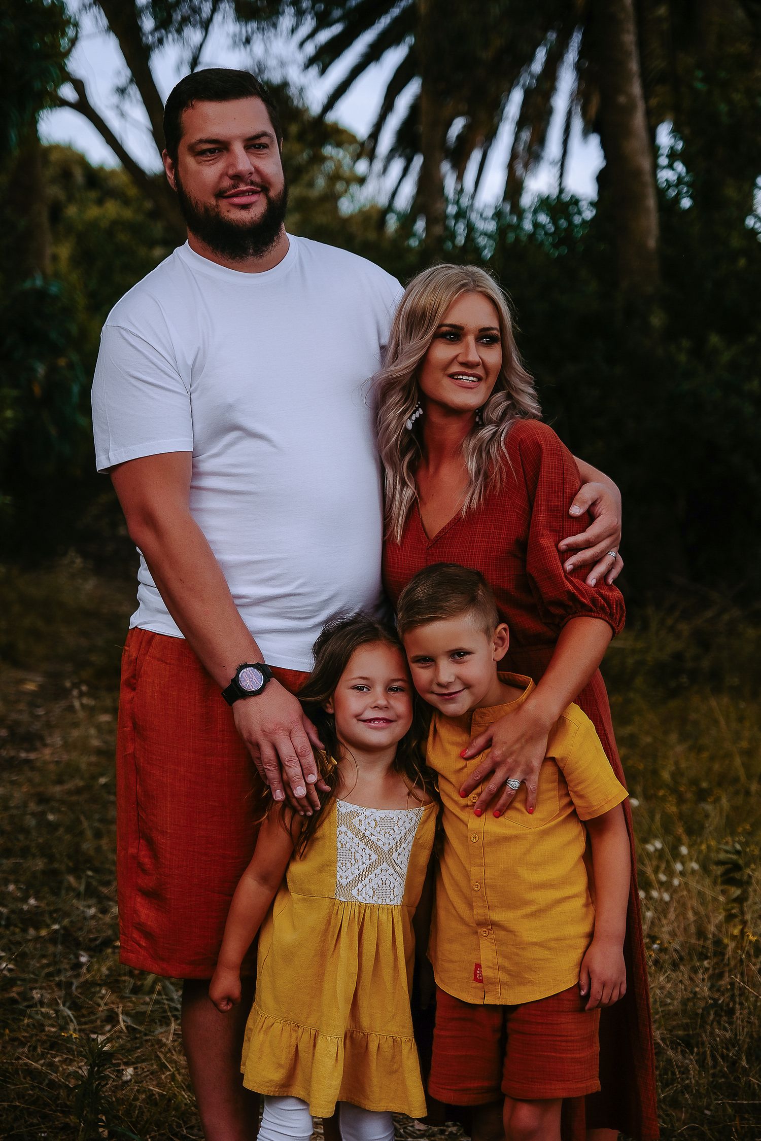 Family of four posing together for a portrait in a wooded setting.