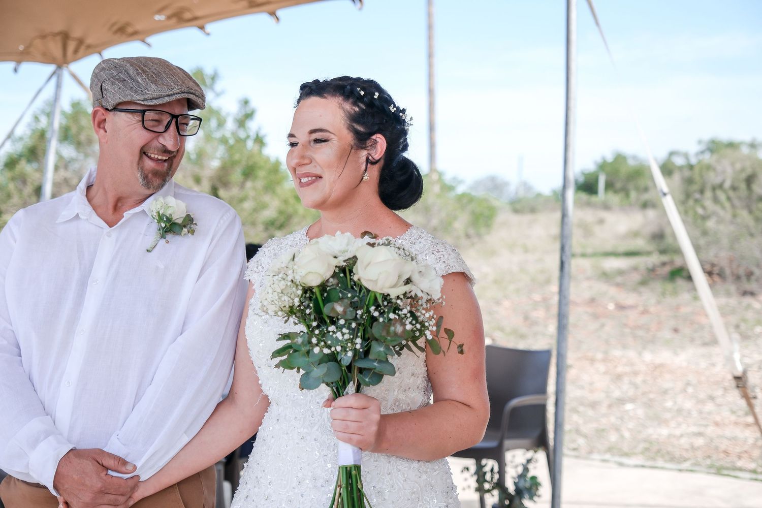 Outdoor wedding ceremony under a tent with couple sharing a joyful moment.