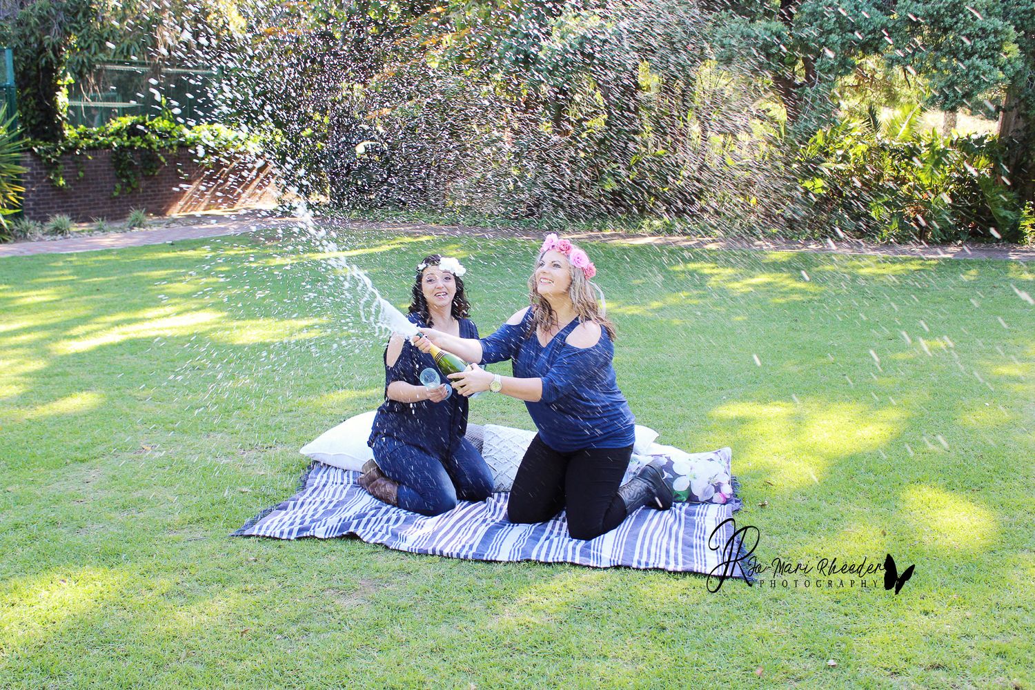 Two people having fun splashing water while sitting on a picnic blanket in a garden.