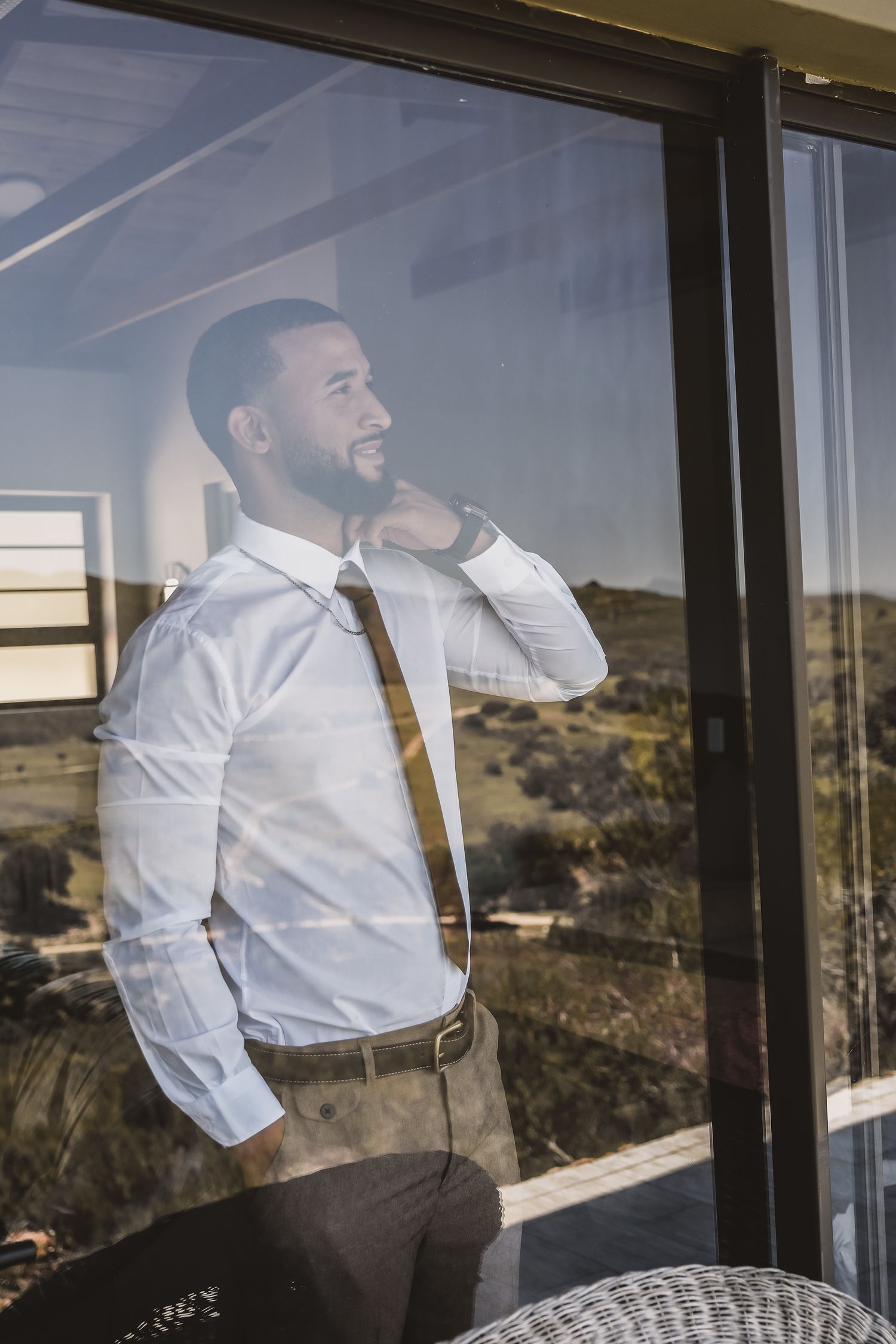 A person in business attire smiling while looking through a window with scenic landscape views.