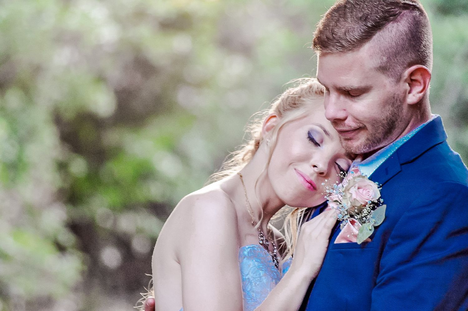 A romantic wedding portrait showing a tender embrace with pink flowers in a garden setting.
