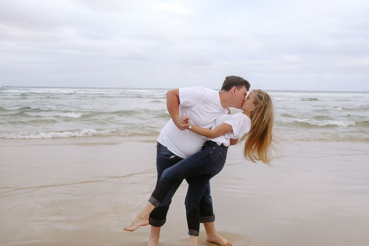 Romantic beach scene with couple dancing in casual attire.
