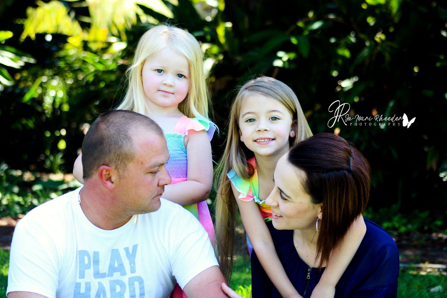 Outdoor family portrait in lush garden setting with bright natural lighting.