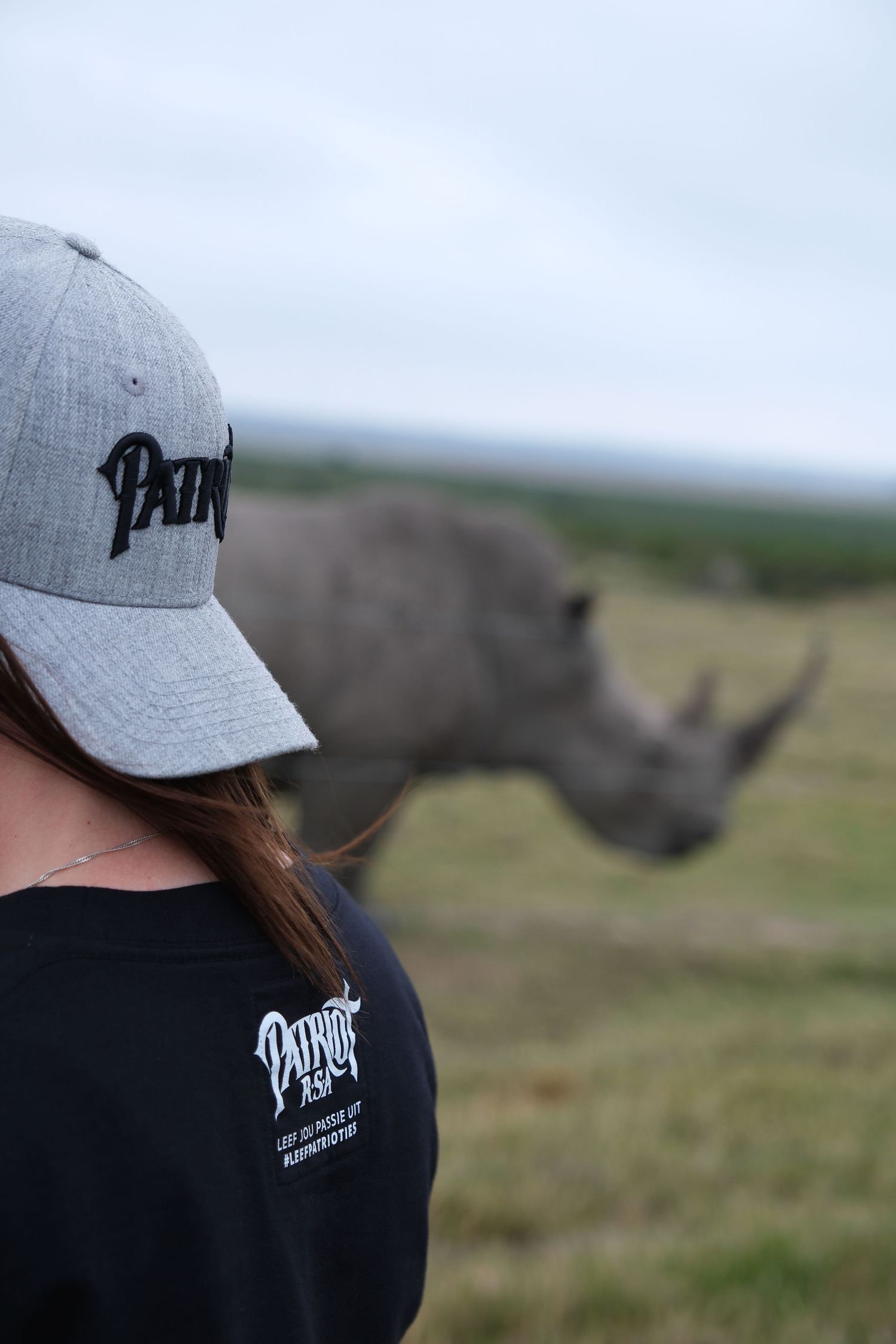 A grey baseball cap and dark shirt against a blurred rhinoceros in the background.