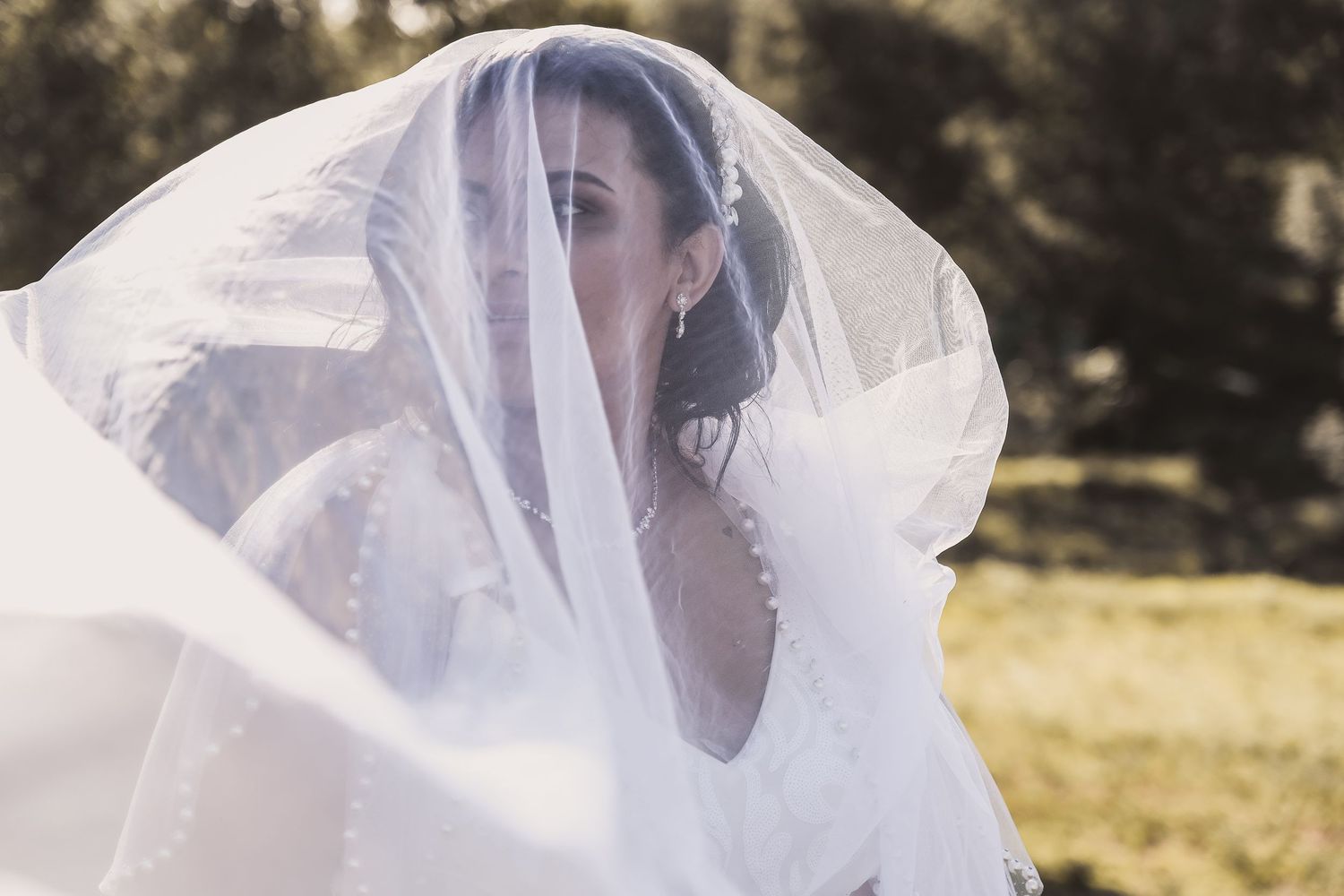 Ethereal bridal portrait with flowing white veil catching the sunlight in an outdoor setting.