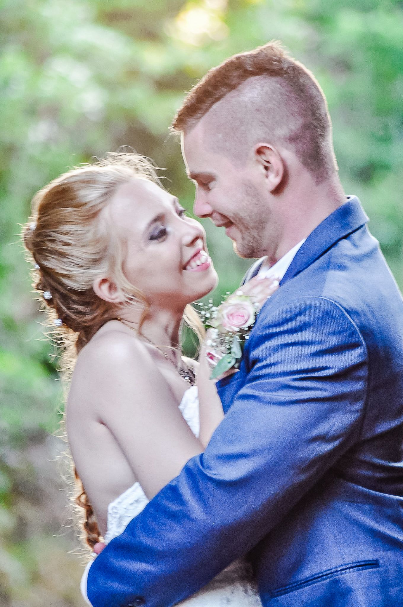 A joyful wedding couple sharing an intimate moment in a sunlit outdoor setting.