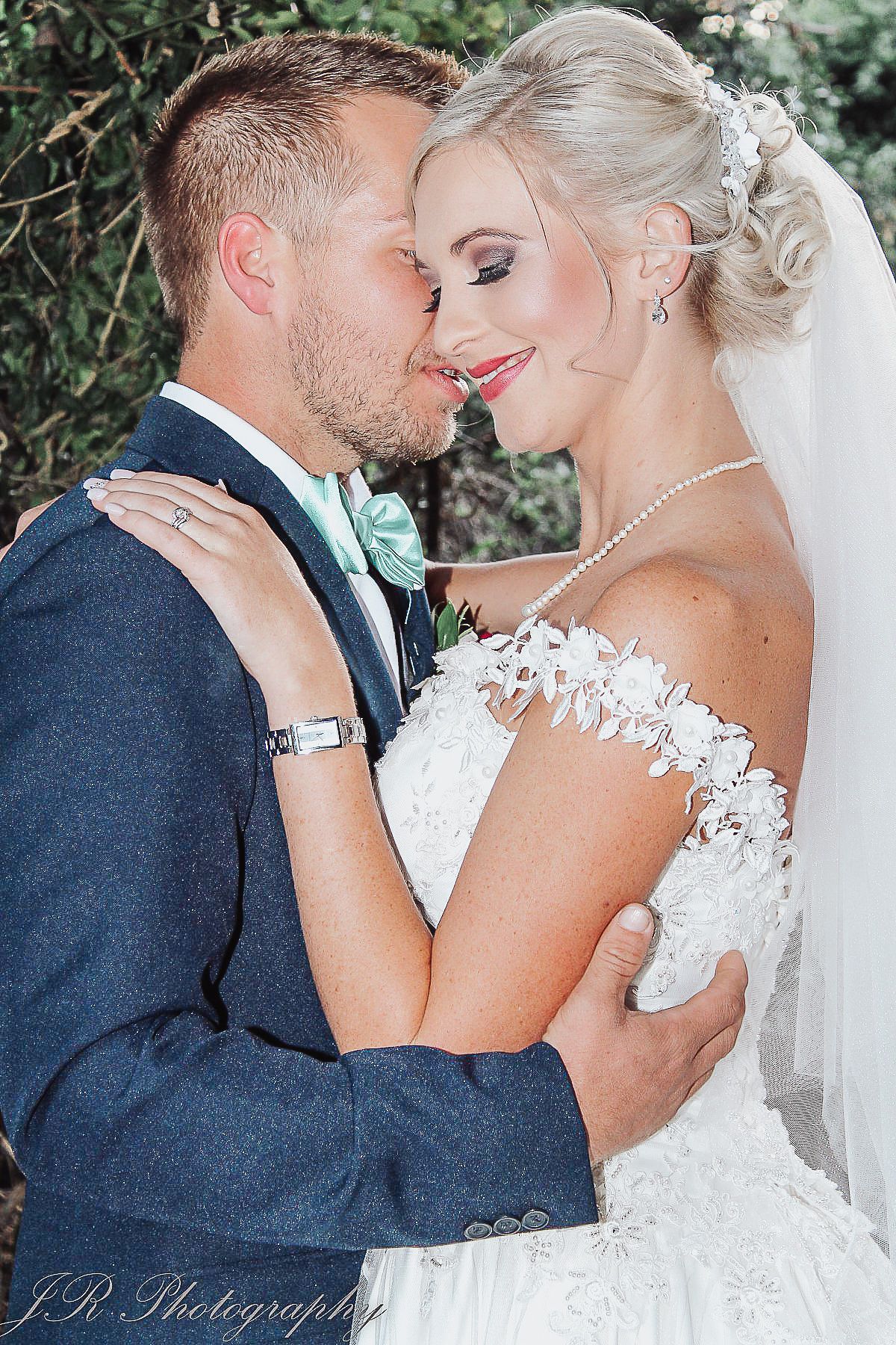 Close-up of a tender wedding moment with bride in lace dress and groom in navy suit.