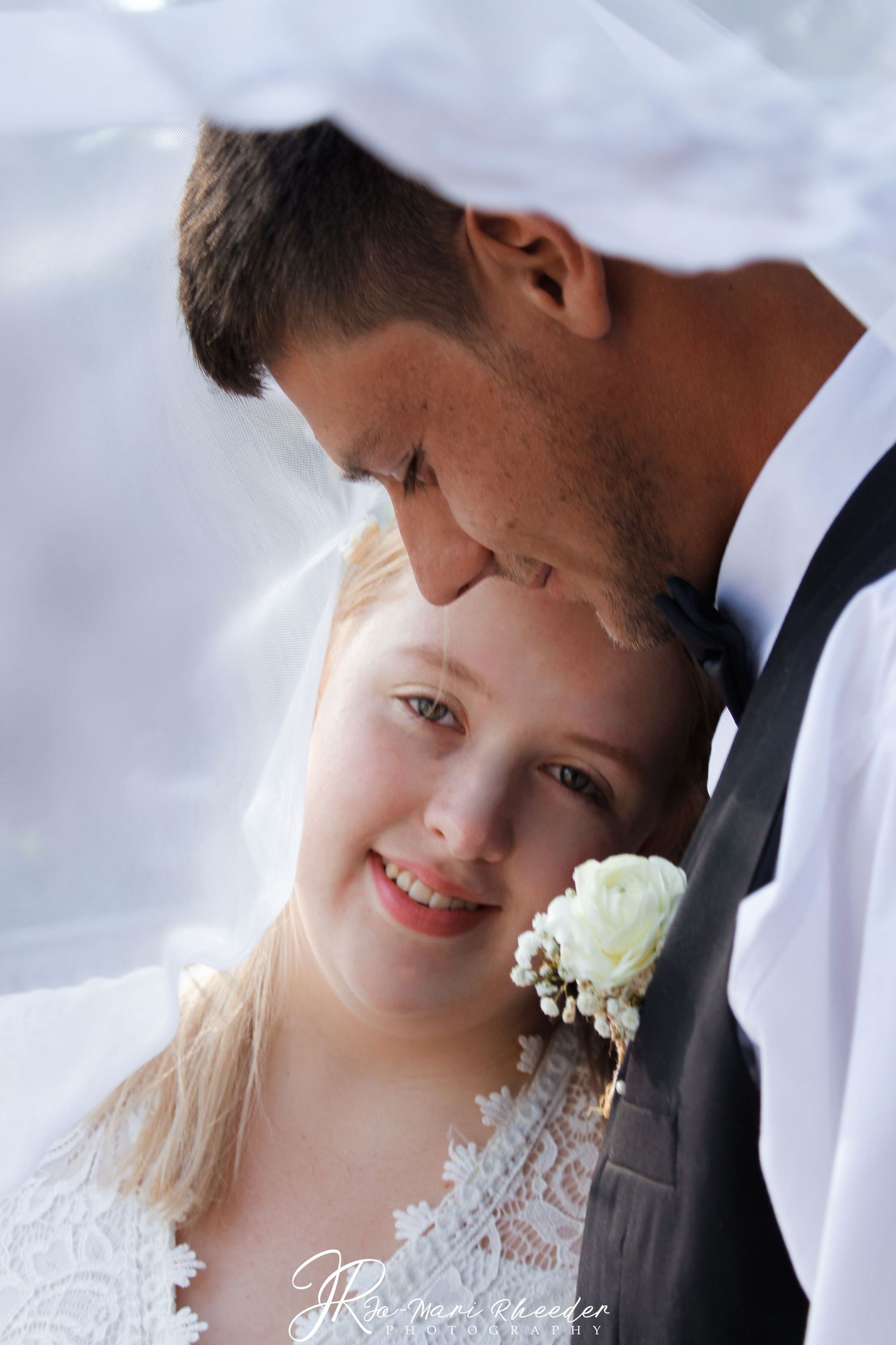 Intimate wedding portrait captured under a flowing white veil in soft lighting.