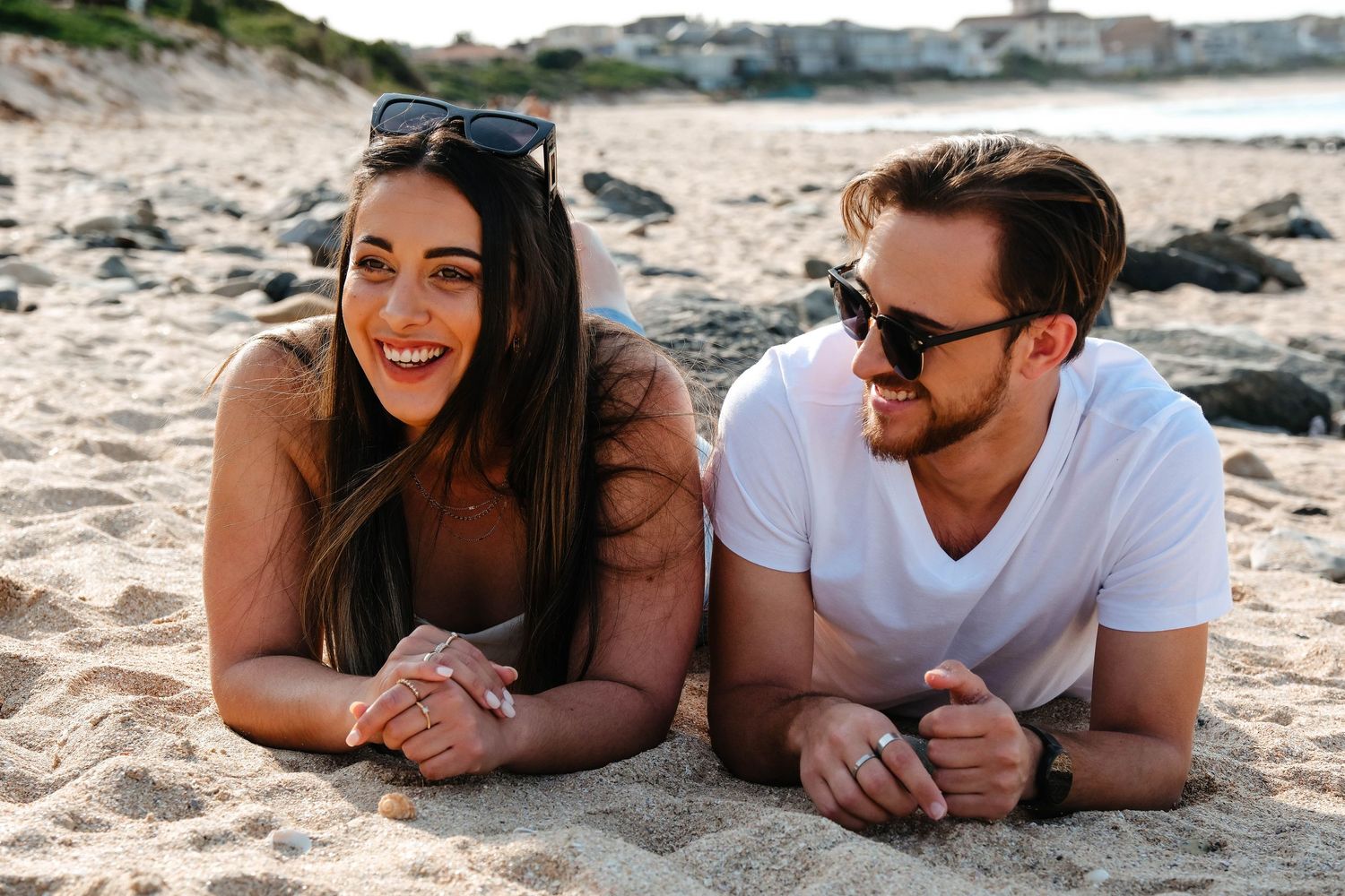 Couple lying on beach sand together laughing and enjoying sunny day.