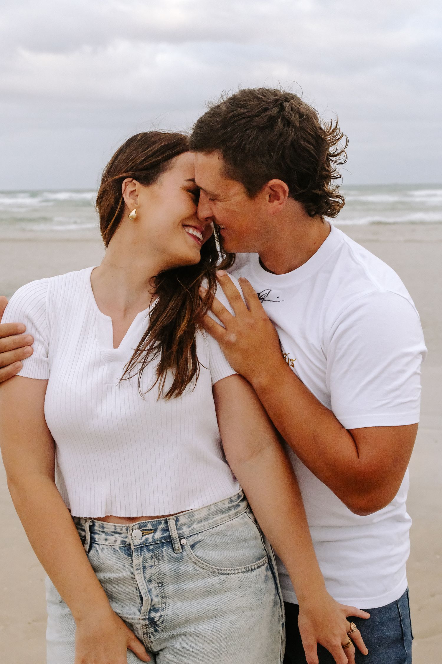 Affectionate couple sharing intimate moment on beach with ocean backdrop.