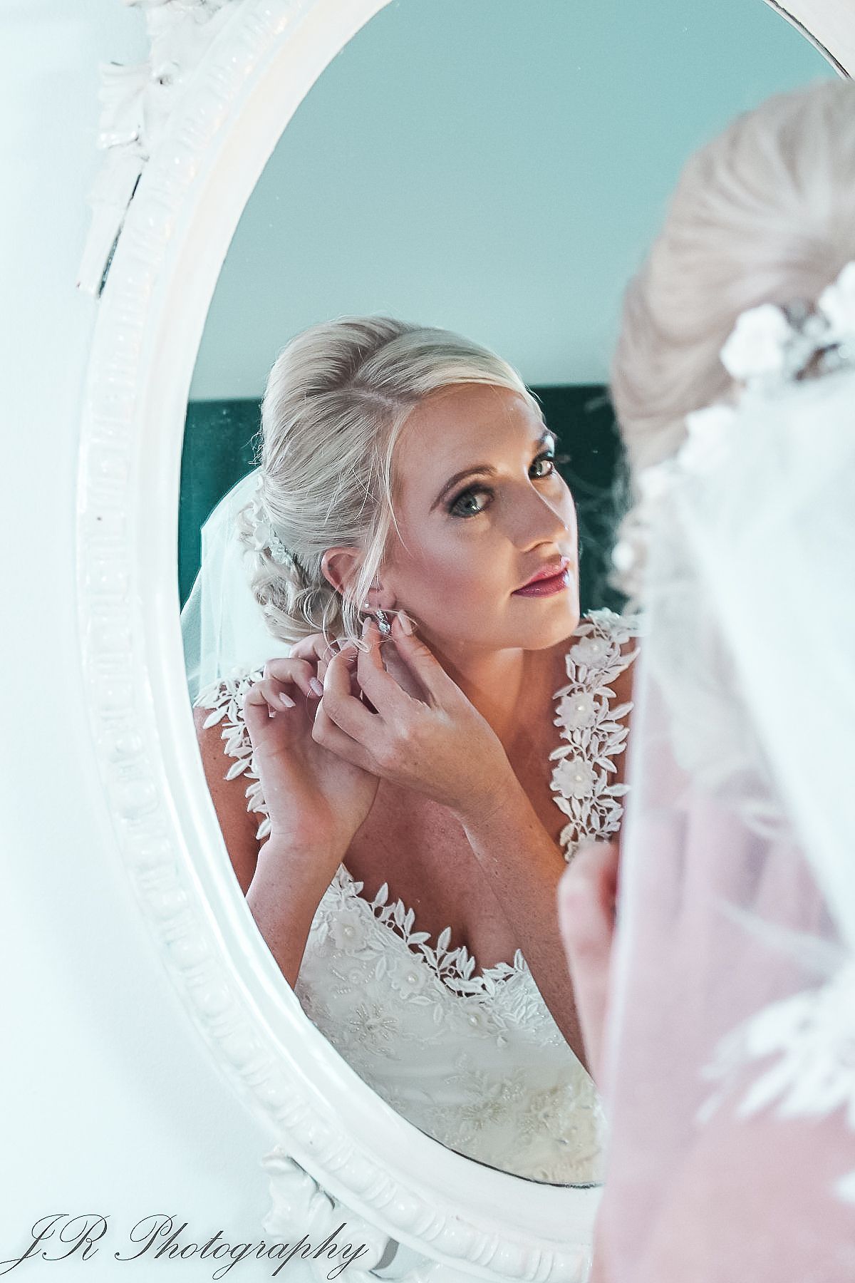 Wedding portrait showing an elegant bridal look reflected in an oval mirror with delicate lace dress details.