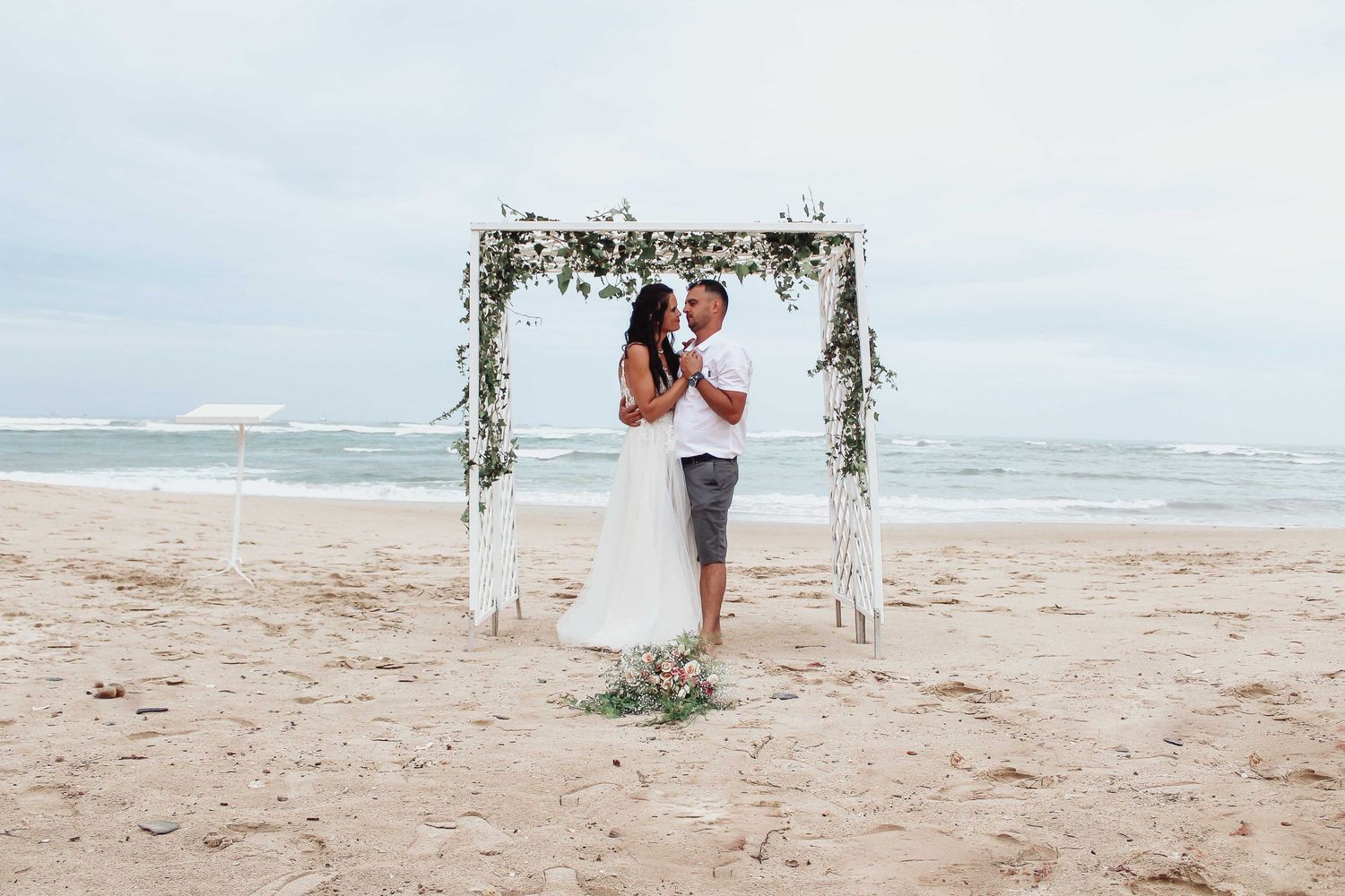 A wedding ceremony setup on the beach with a floral arch and ocean backdrop.