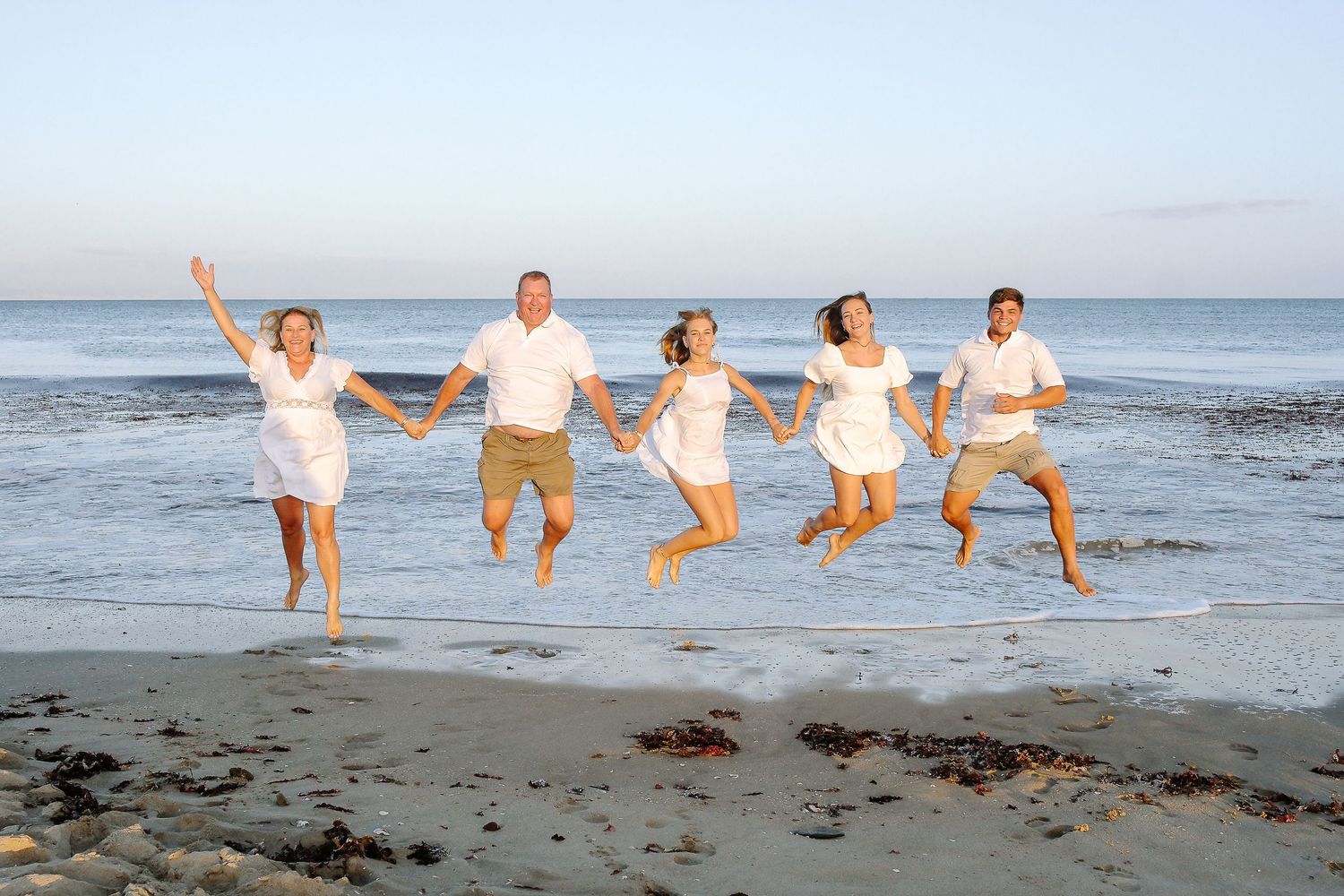 Group of people jumping in unison at the beach during sunset with ocean waves in background.