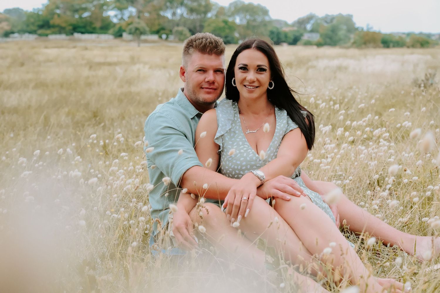 Couple sitting together in sun-lit meadow with wild flowers.