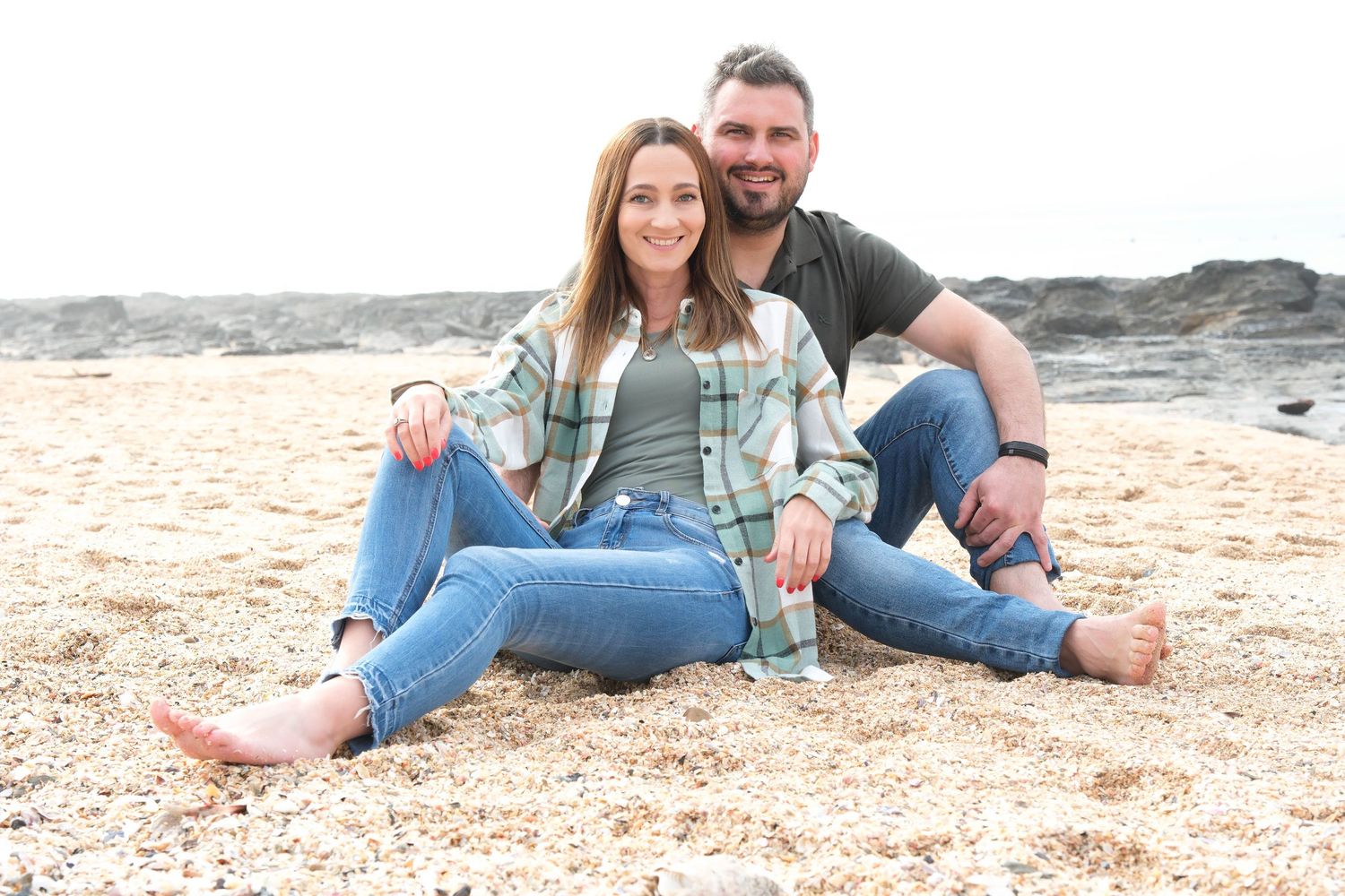 Casual couple relaxing together on sandy beach wearing matching plaid shirts.
