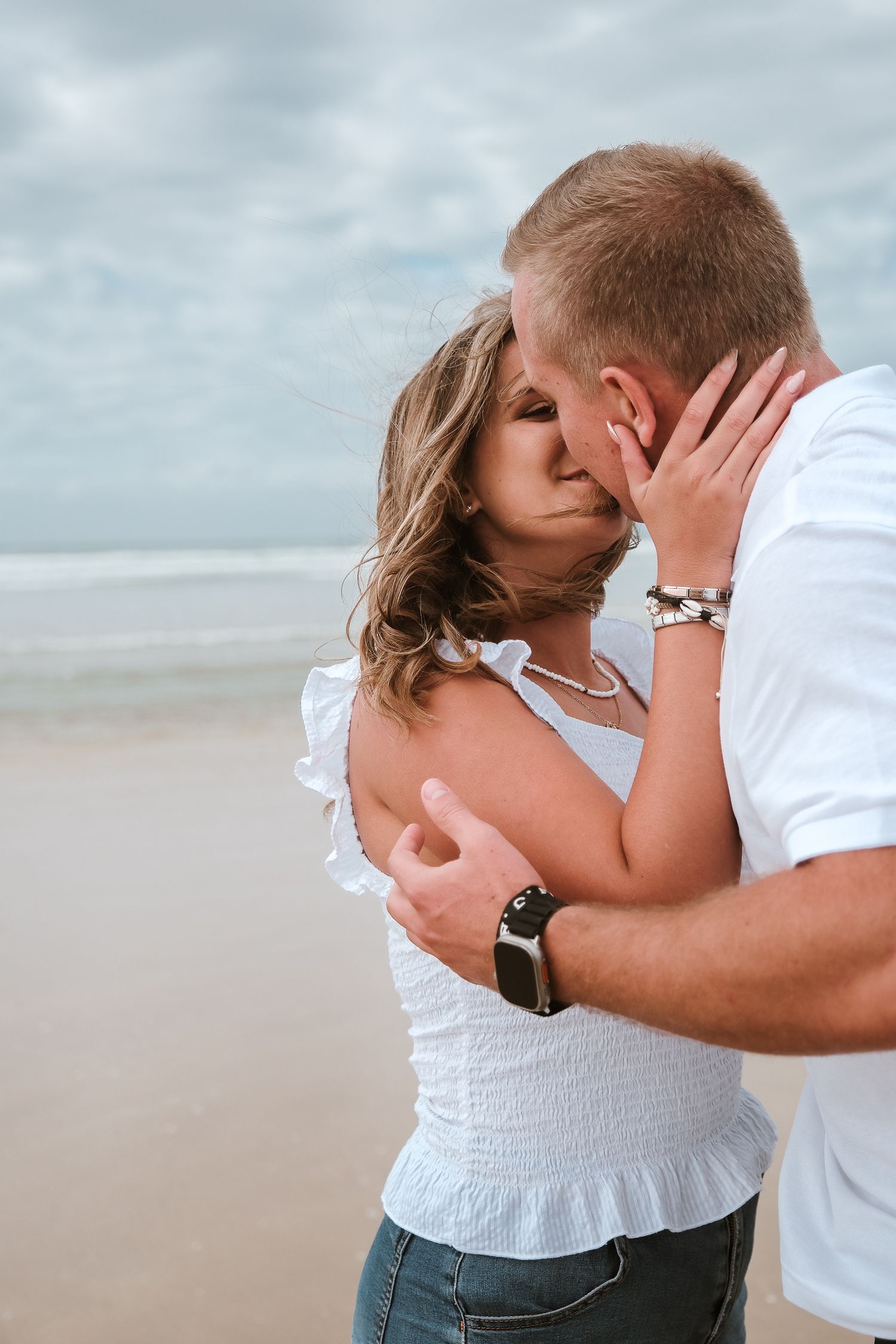 Tender embrace between couple on beach with overcast sky.
