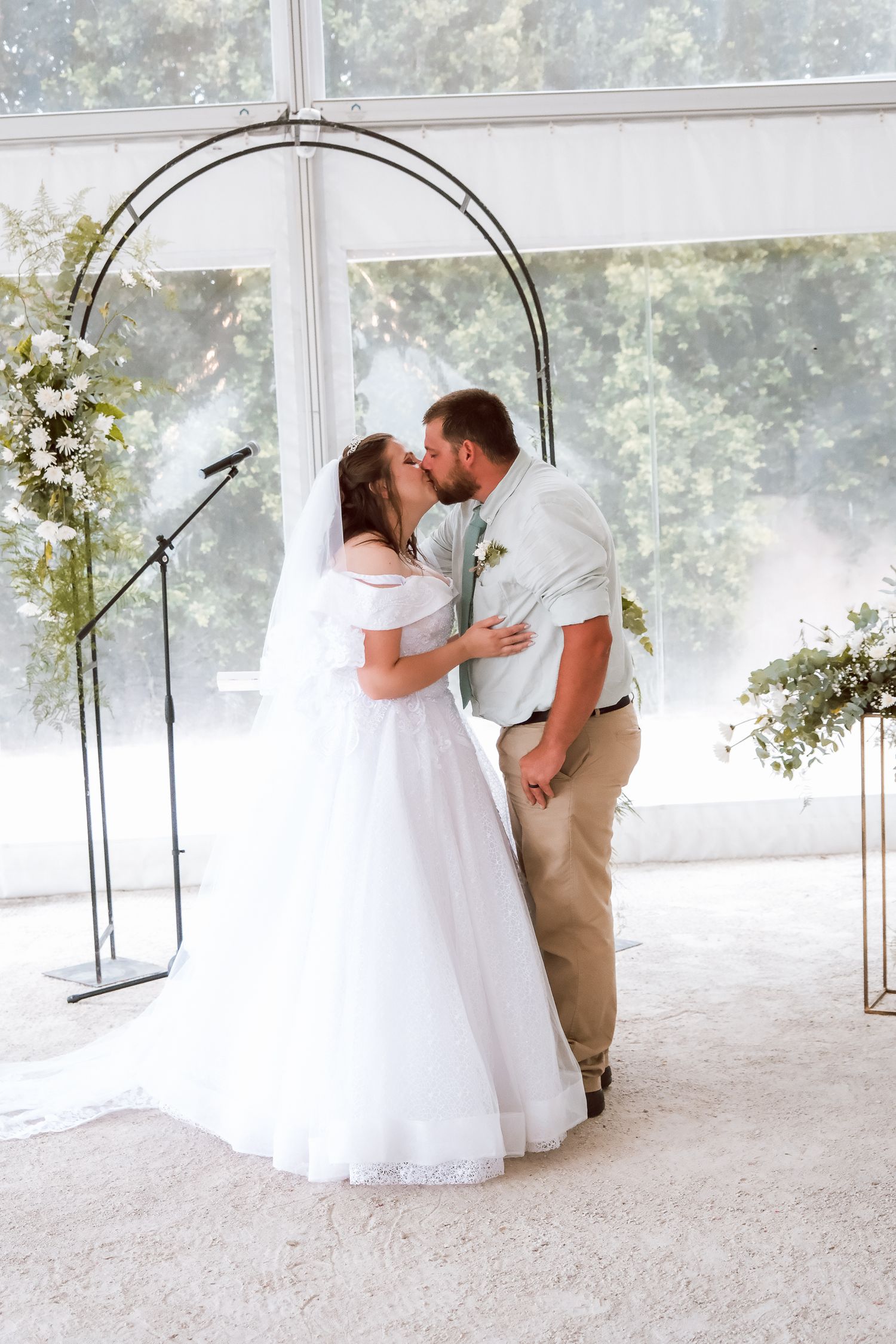 Romantic wedding kiss under a floral archway during an indoor ceremony.