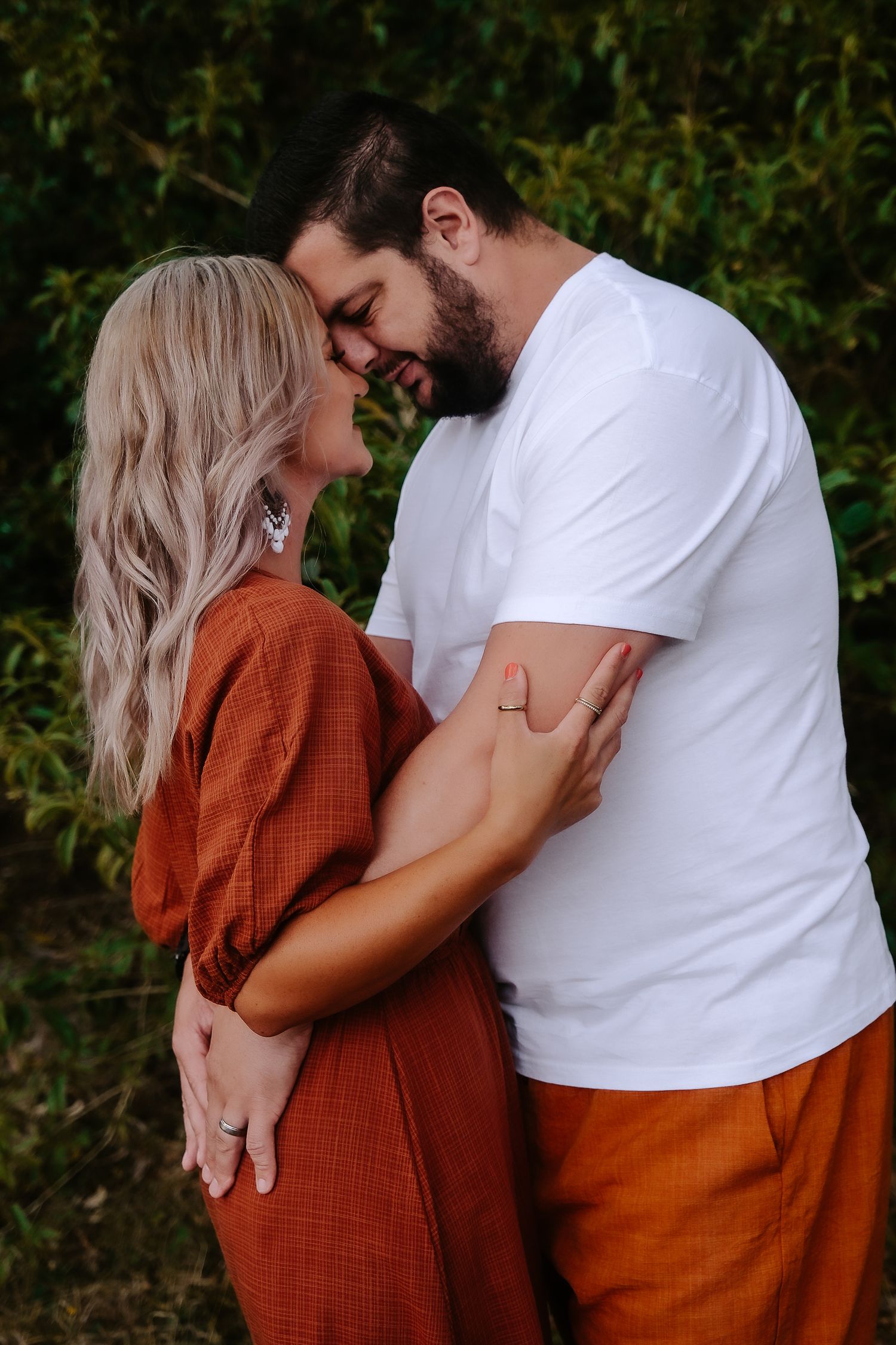 Romantic couple in matching rust-colored and white outfits share an intimate moment against a green garden backdrop.