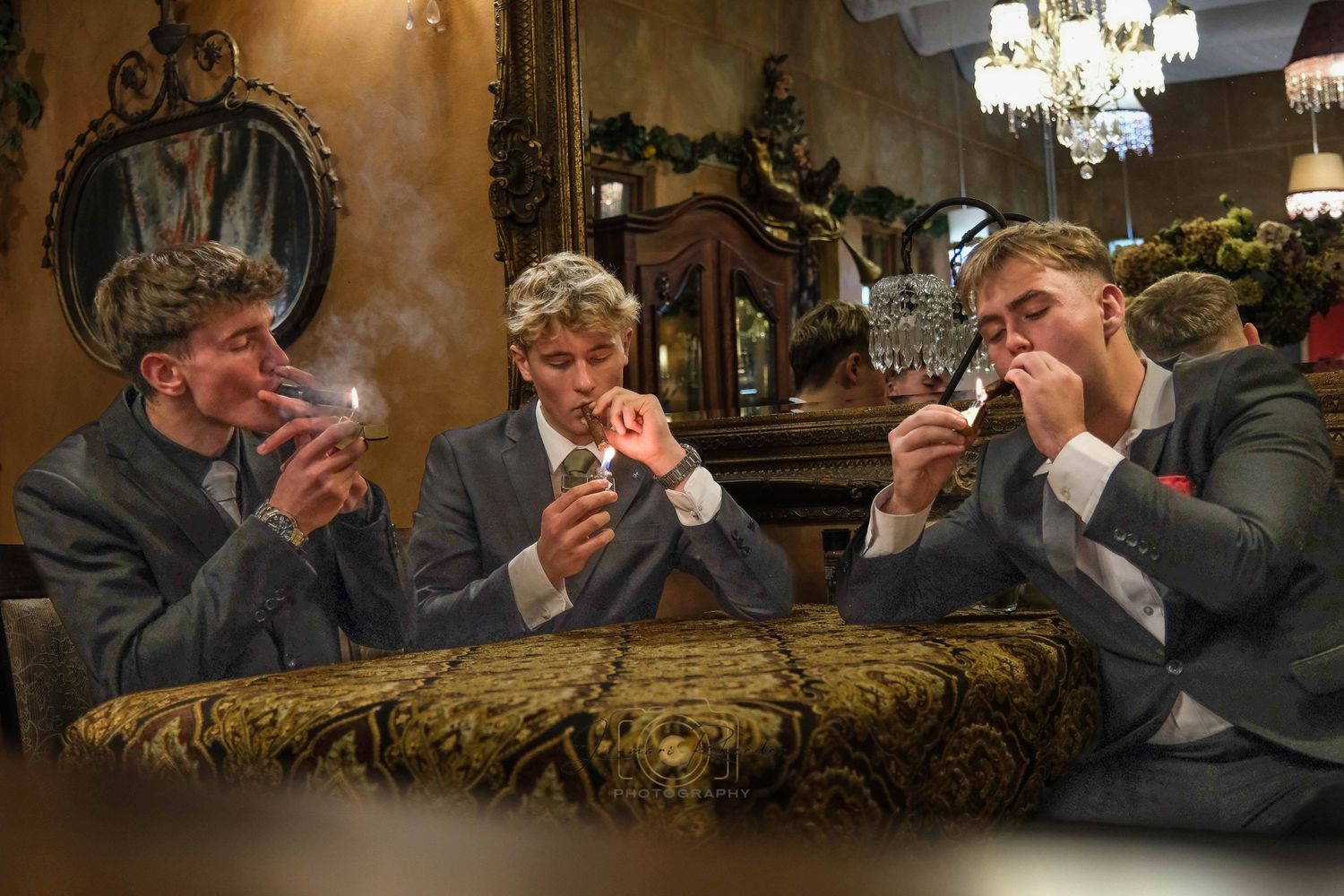 Three people enjoying cigars in an ornate room with chandelier lighting.