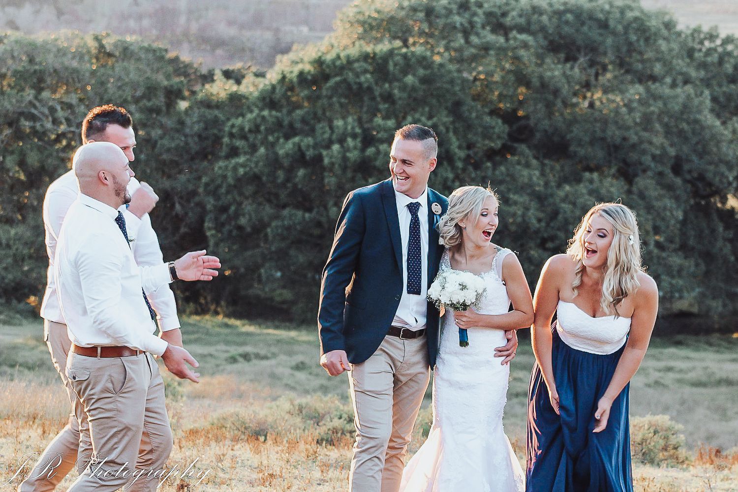 Wedding party laughs together during outdoor golden hour photo session.