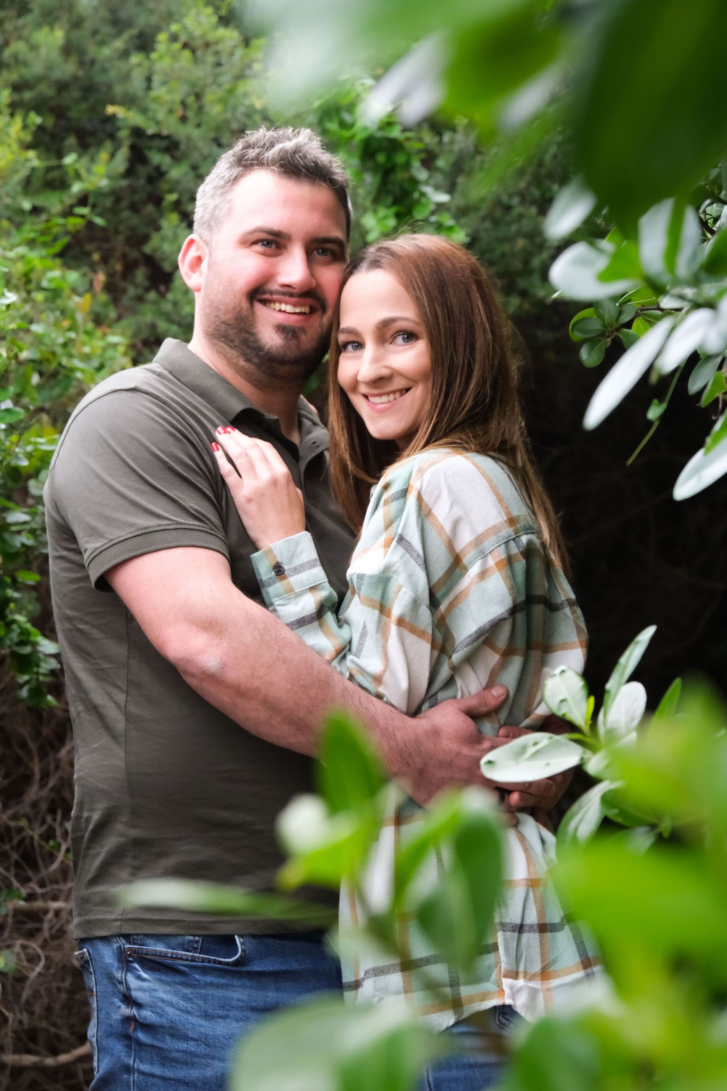 Happy couple embracing among green foliage in outdoor portrait.