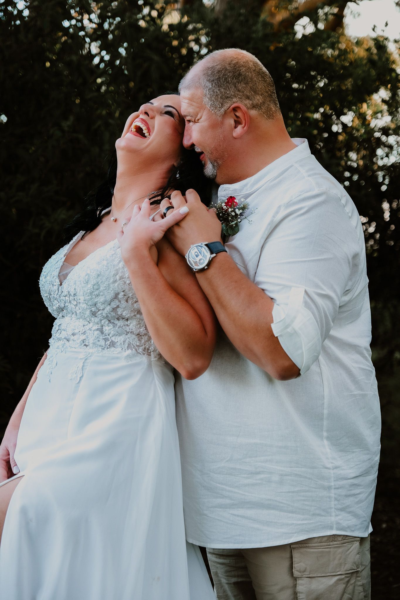A joyful candid wedding moment between a couple outdoors, showing genuine laughter and happiness.