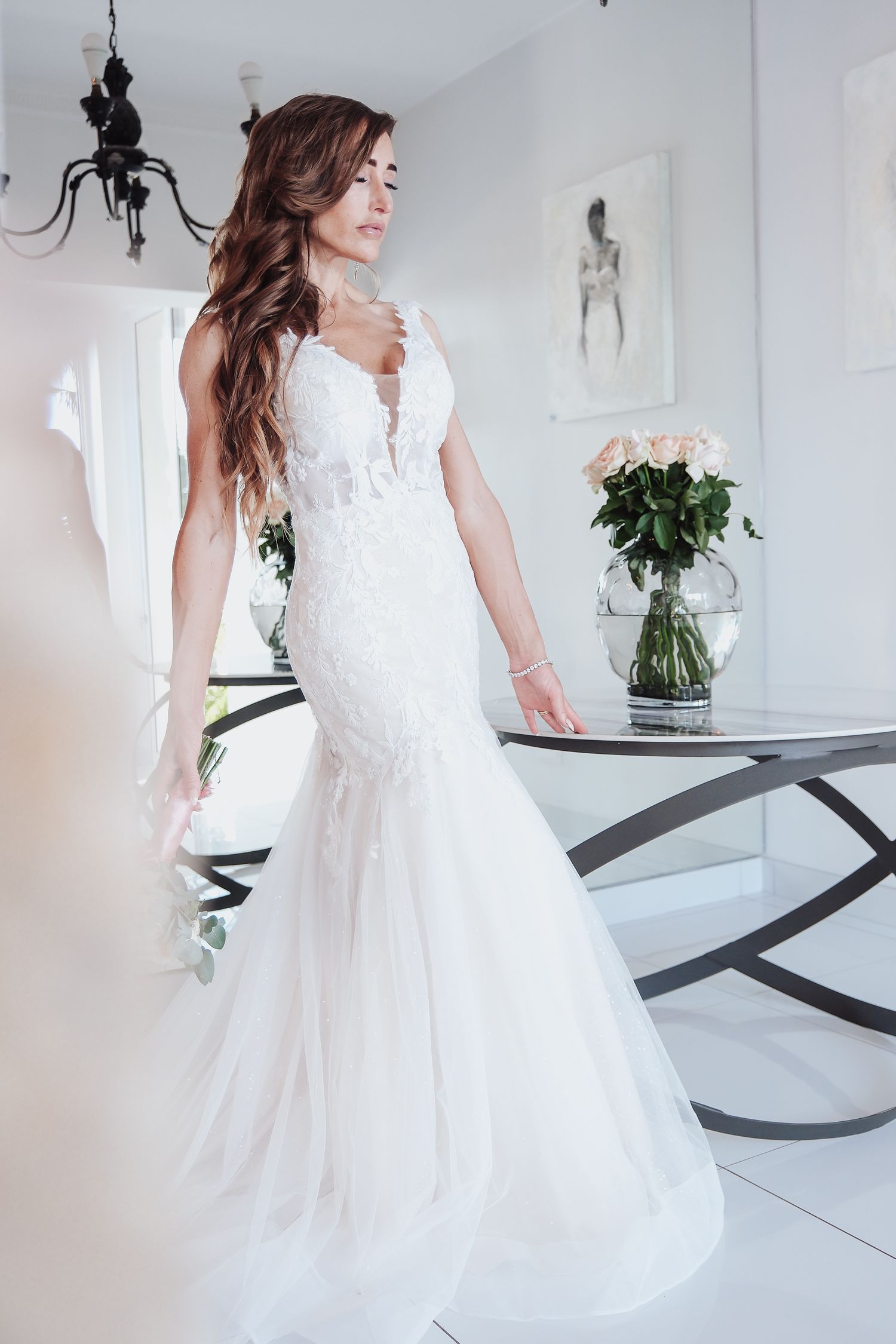 Stunning mermaid style wedding gown with lace details in bright white room.