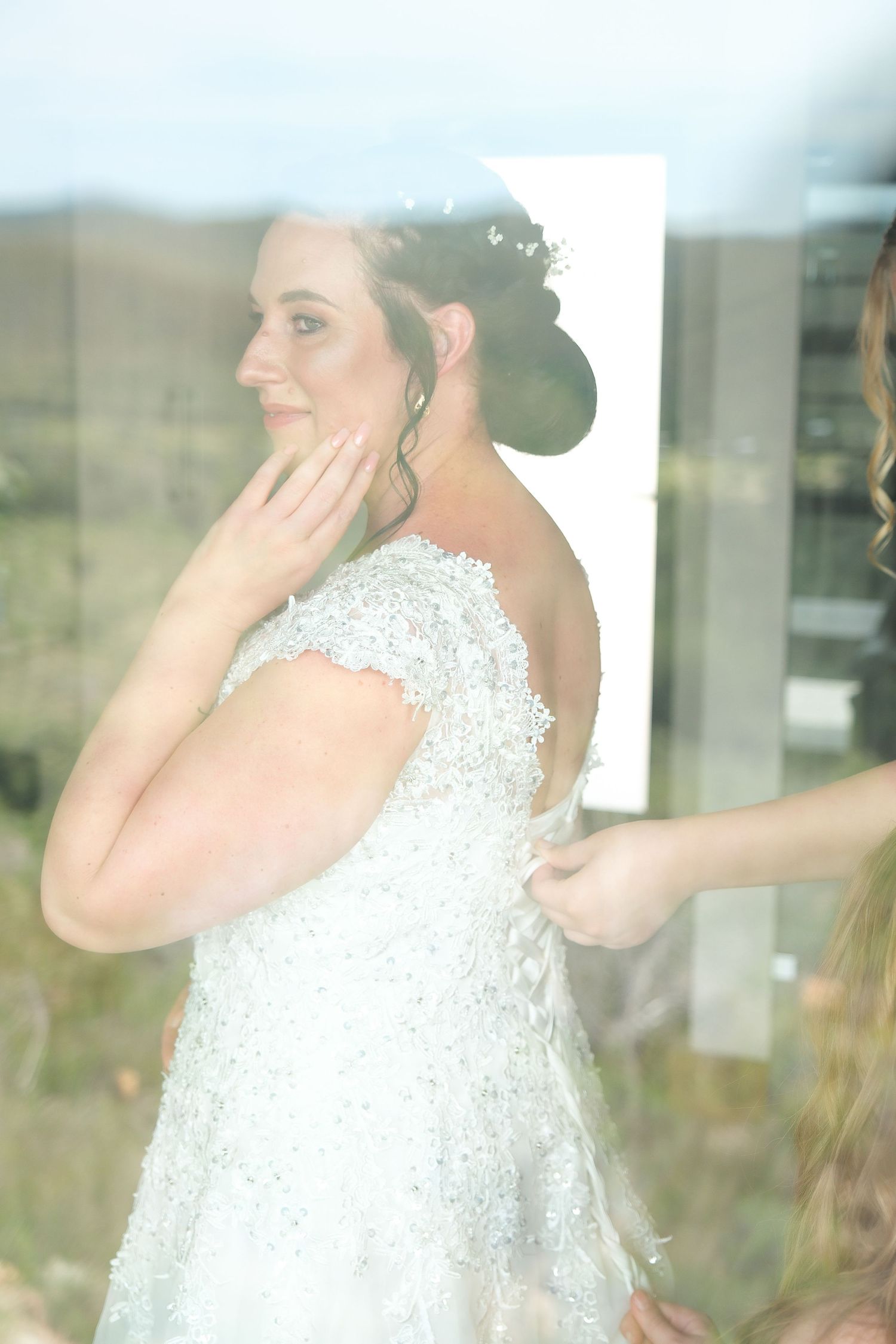 Soft dreamy view through window of bride in lace dress preparing for wedding.
