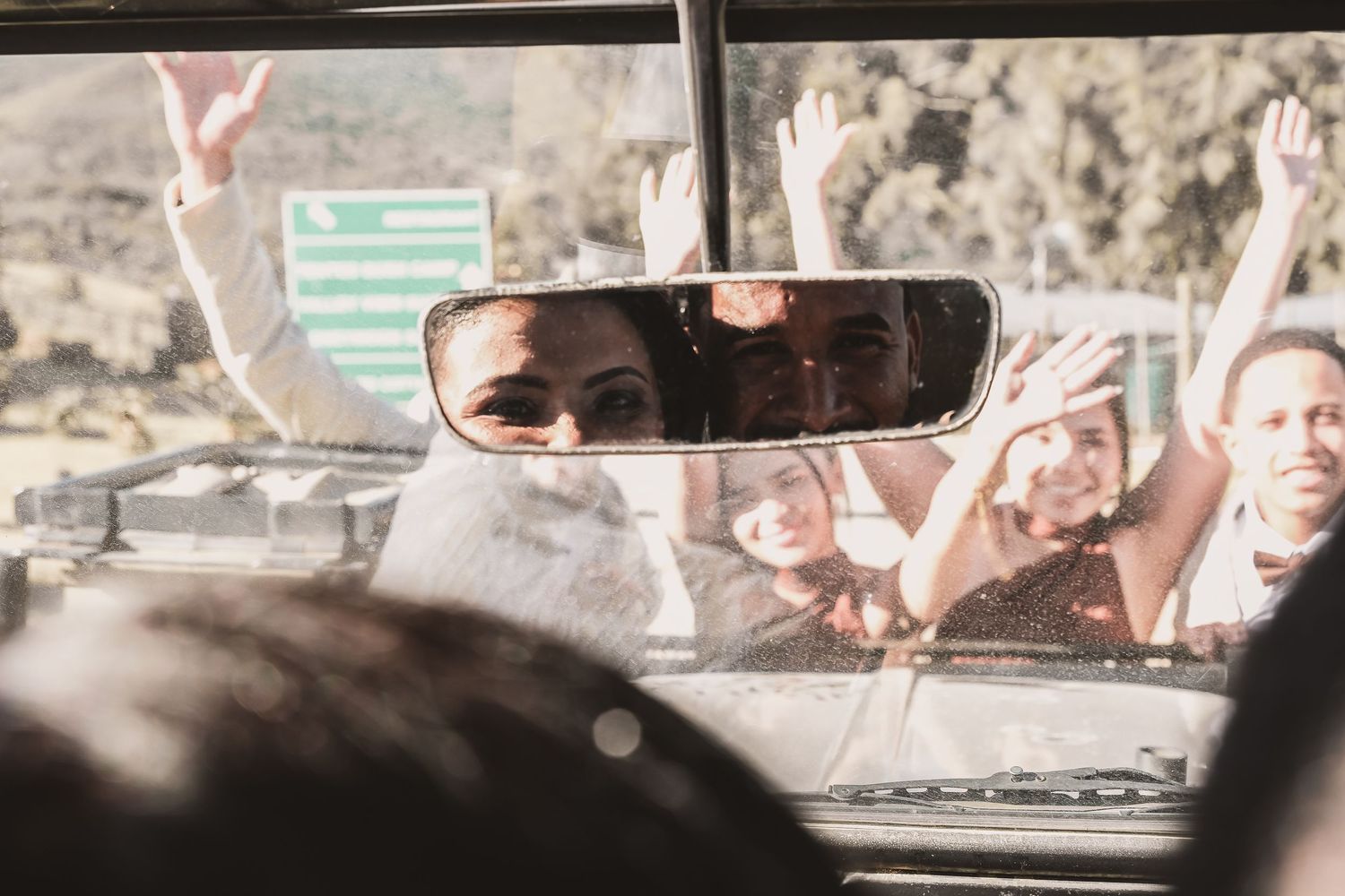 View through a car's rearview mirror showing celebration and raised hands.