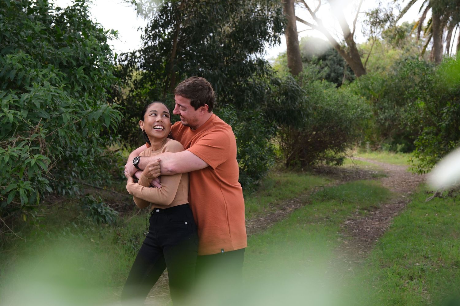 Playful couple embracing on nature trail surrounded by lush greenery.