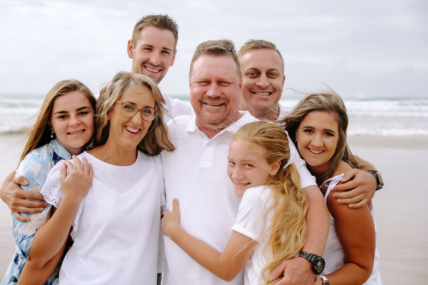 A group enjoying a casual day at the beach together, dressed in light colors against an overcast sky.