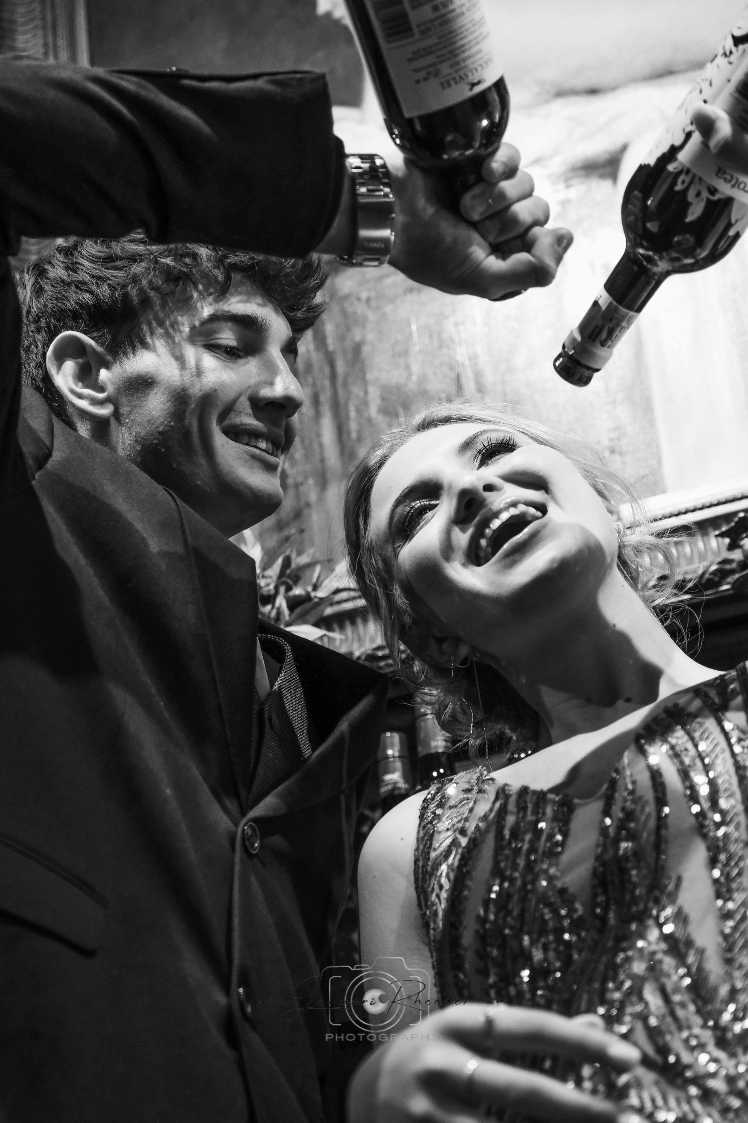Black and white candid party photo of couple laughing with champagne bottles.
