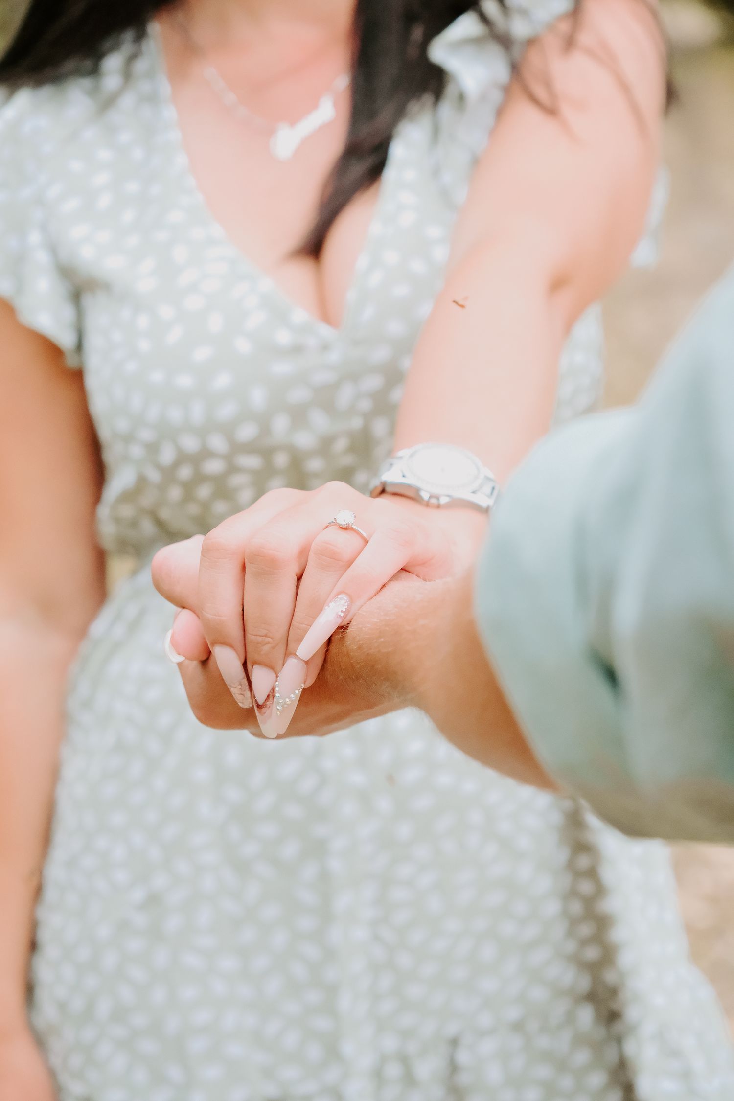 A close up view of intertwined hands showing off a new engagement ring.
