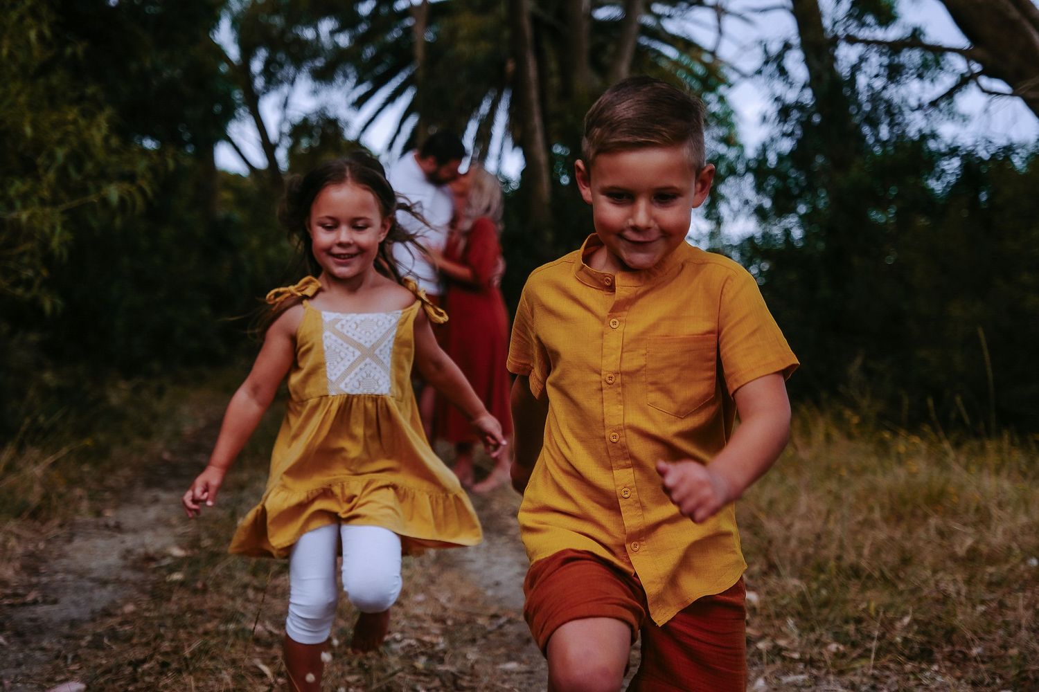 Two children in yellow outfits running together on a nature path.
