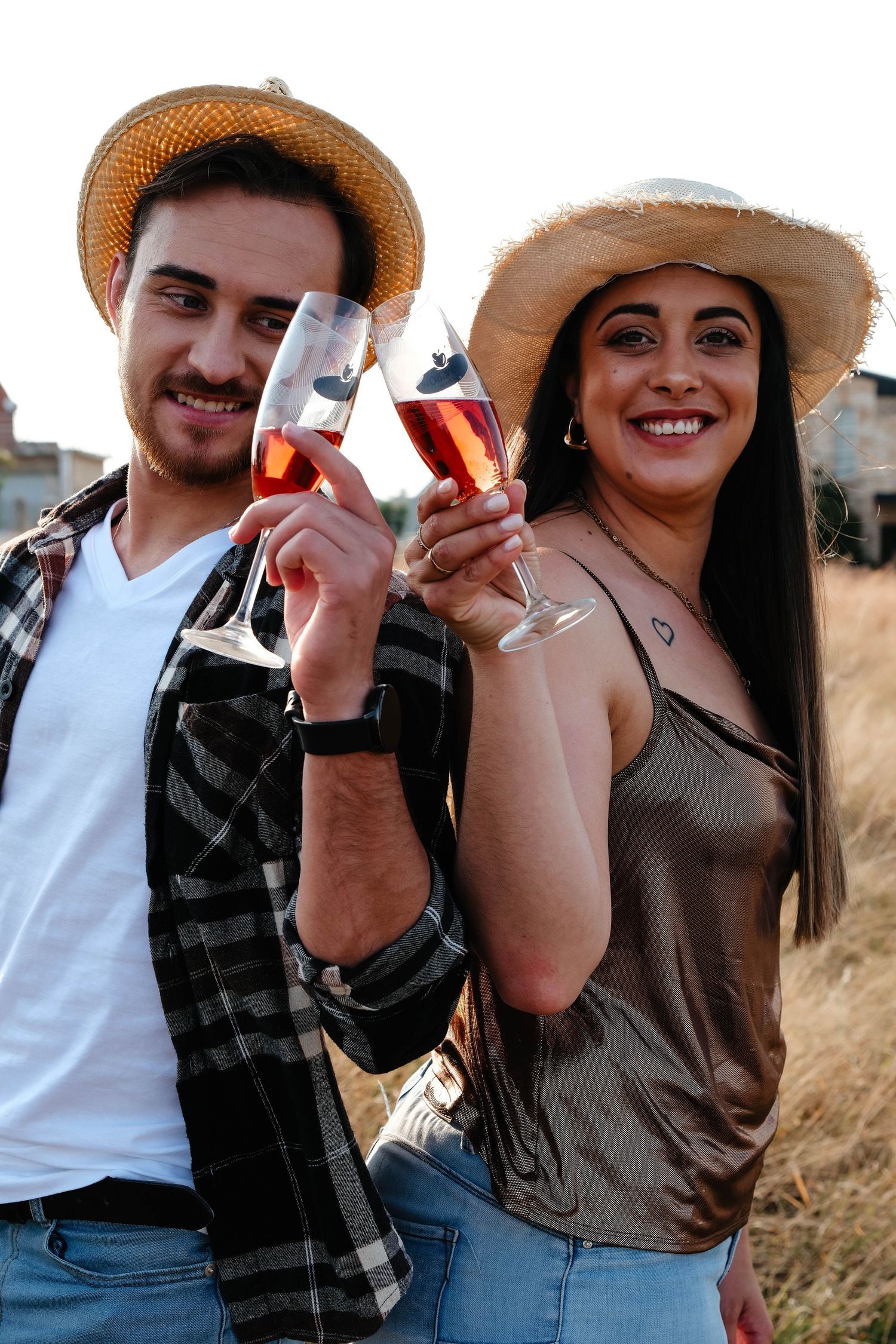 Two people in straw hats toasting with glasses in an outdoor setting.