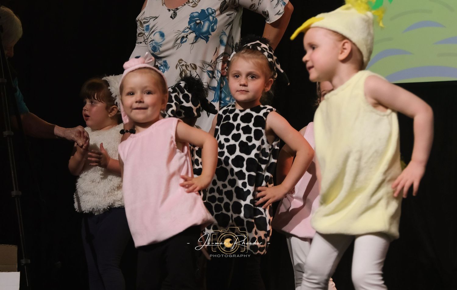Young children perform together on stage in colorful outfits during a dance show or recital.