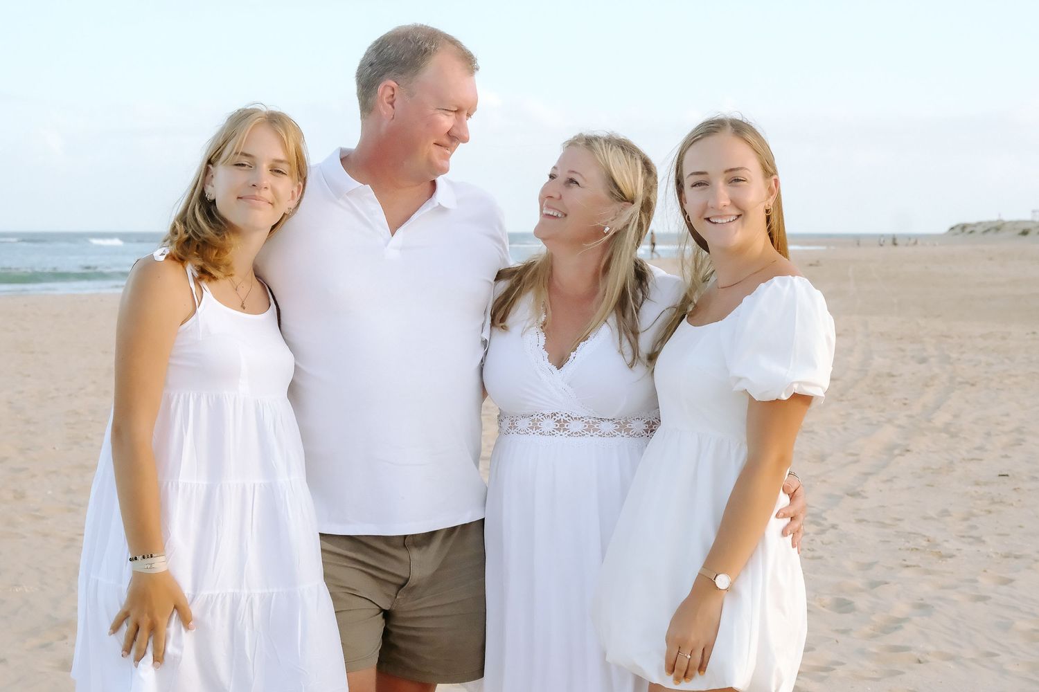 A family group in white outfits posing together on a sandy beach.