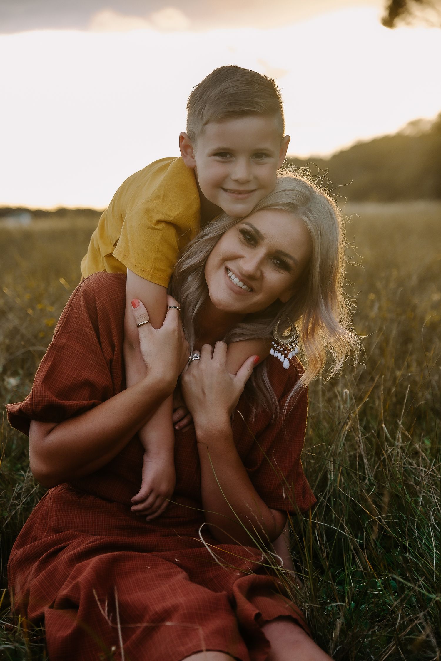 Intimate portrait of parent and child embracing in a field at sunset.